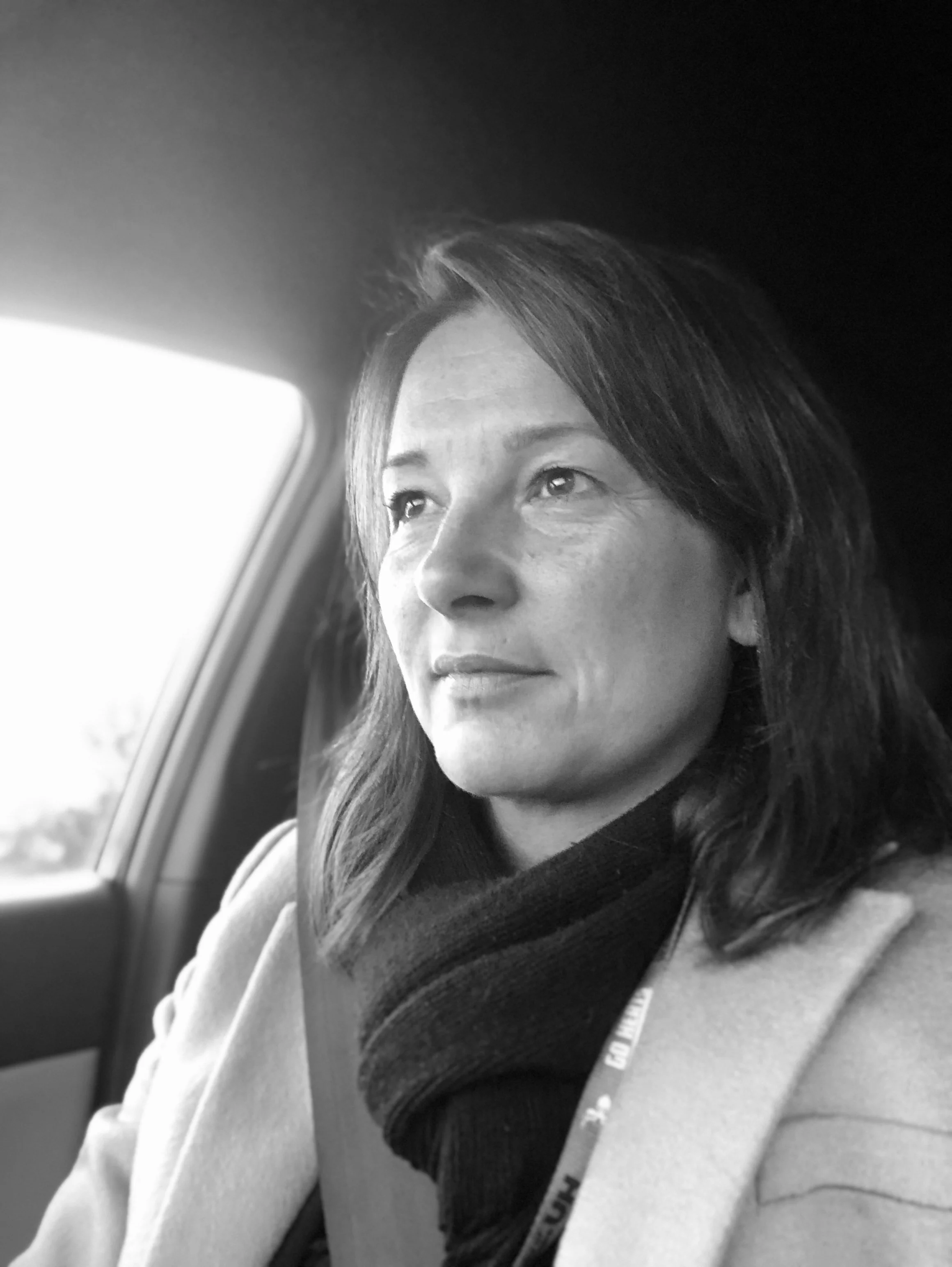 A woman with medium-length hair sitting in a car, looking out the window.