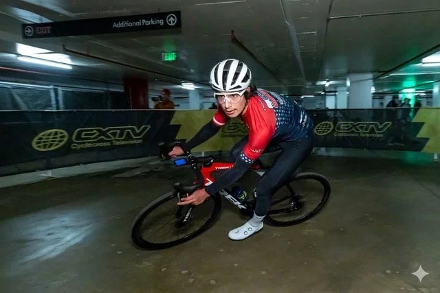 Cyclist in an indoor parking garage riding a black and red bicycle, wearing a white helmet, glasses, and a red and blue cycling jersey.