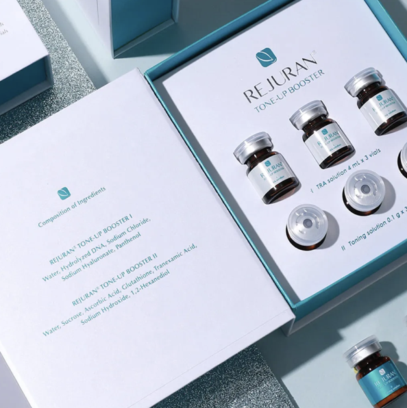 Open box of Rejuran Tone-Up Booster with three small glass bottles inside, each with silver caps and labeled solutions, alongside a leaflet detailing ingredients and usage.