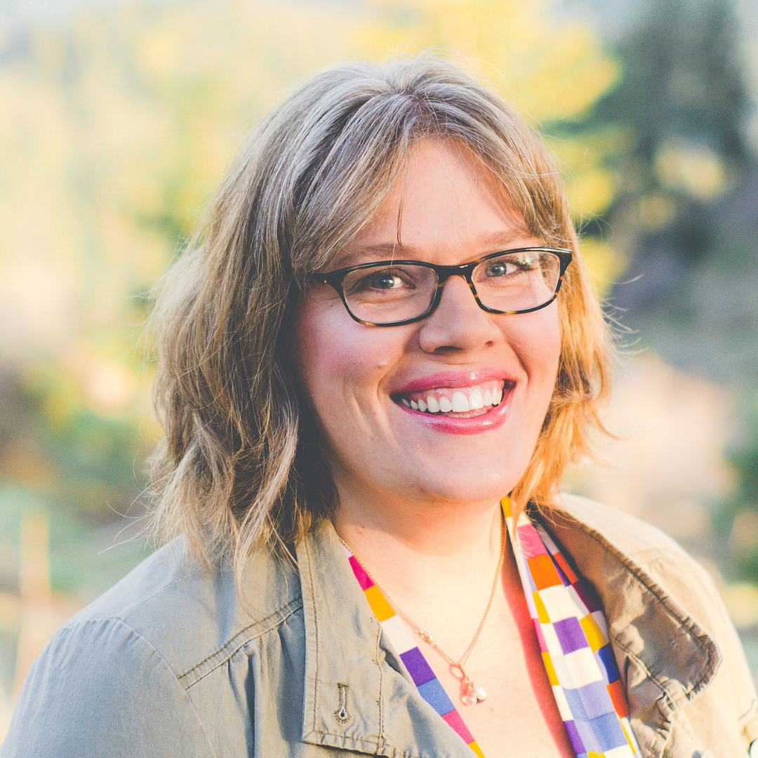 Photo of Amy Simpkins, a smiling woman with wavy dark blonde hair and black framed glasses.