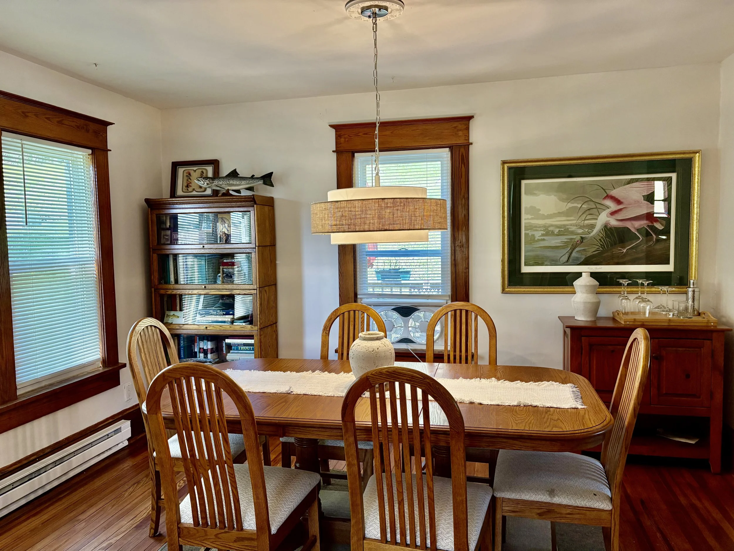 Dining room with wooden table and chairs, large framed picture of a pink flamingo, china cabinet, and decorative fish on the wall.