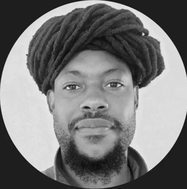 A black-and-white photo of a man with a beard and dreadlocks, wearing a turban and a suit, with a circular banner around his face that says 'GROW UP TOP 50 CANNABIS LEADER' and includes a maple leaf icon.
