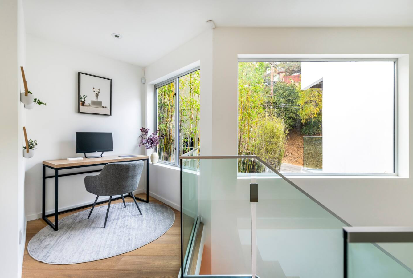 A bright, modern workspace with a desk, gray chair, computer monitor, and window overlooking greenery.