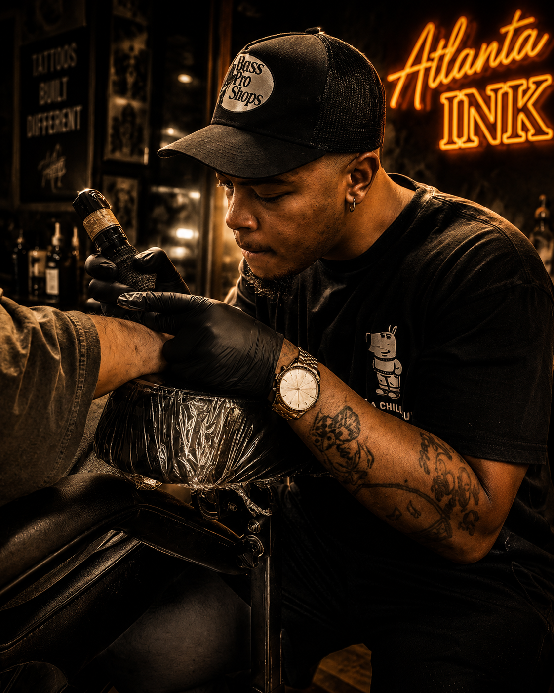 Tattooed tattoo artist wearing a cap, black gloves, and a watch, ink designing a client's arm in a tattoo shop with neon "Atlanta Ink" sign.