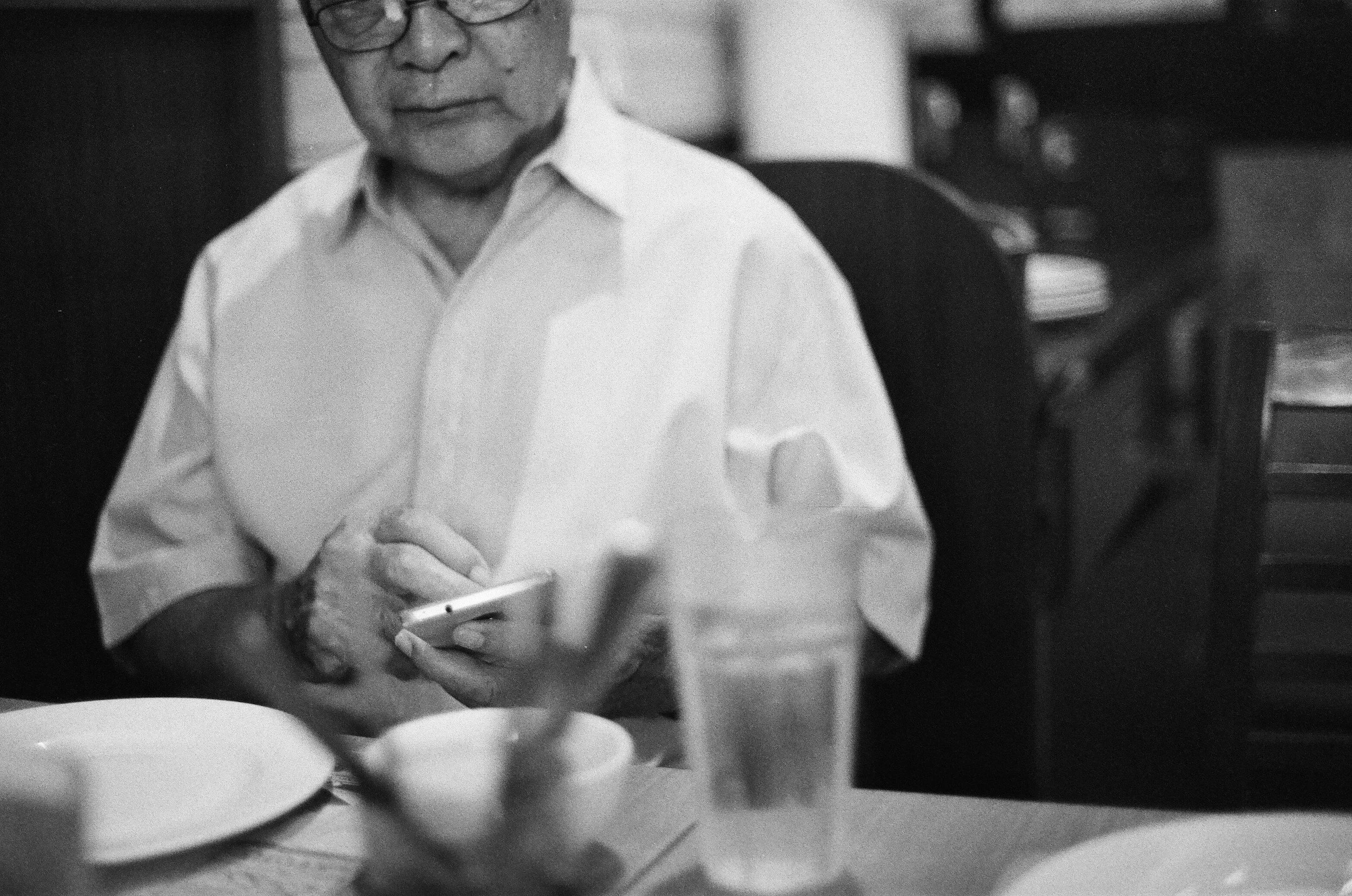 Black and white photo of an Asian senior man in a white shirt on a smart phone