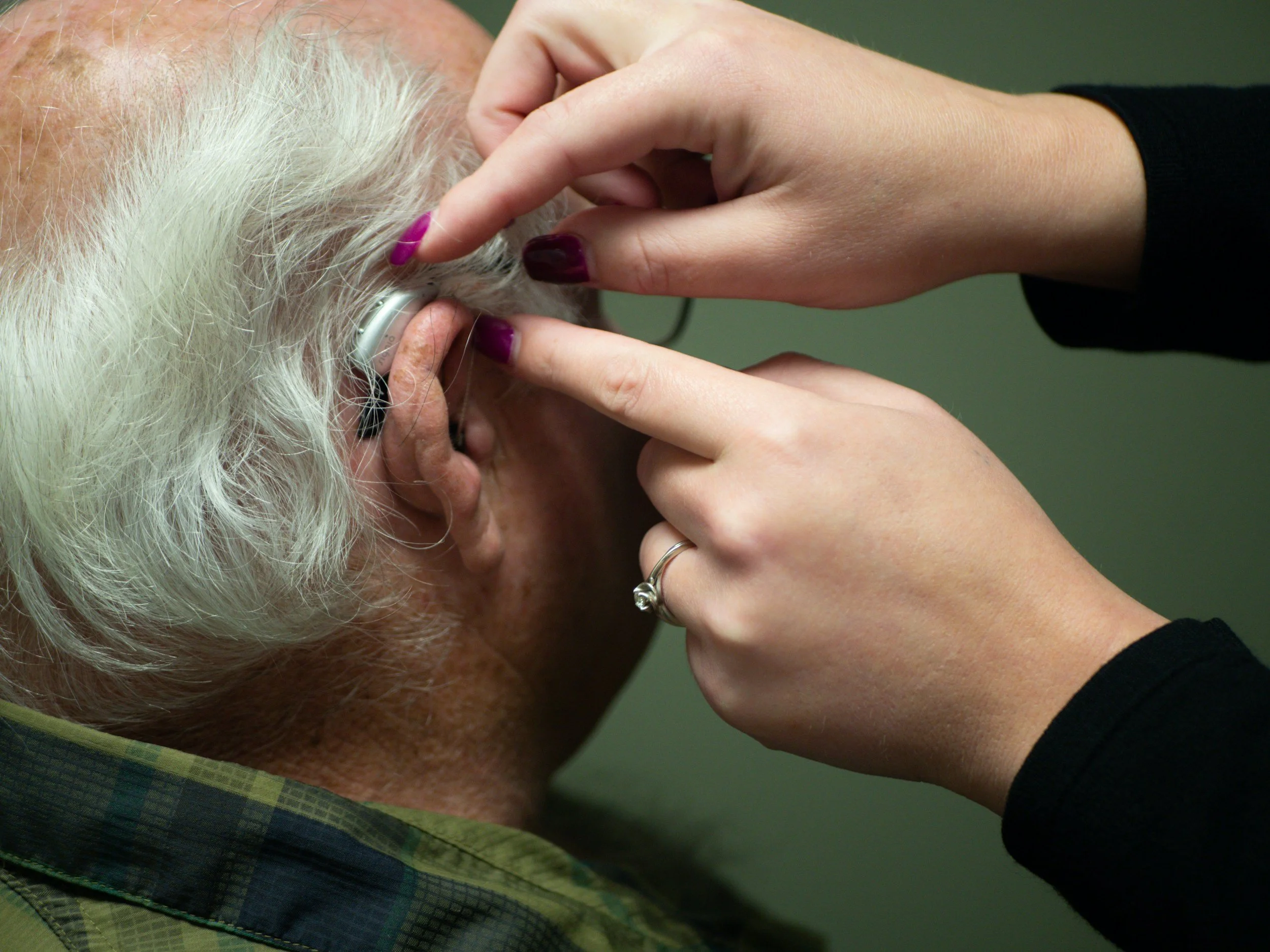 Caregiver fitting hearing aid on senior during hospital discharge checklist.
