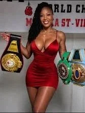 A woman in a red dress standing in front of a boxing-themed background with championship belts.