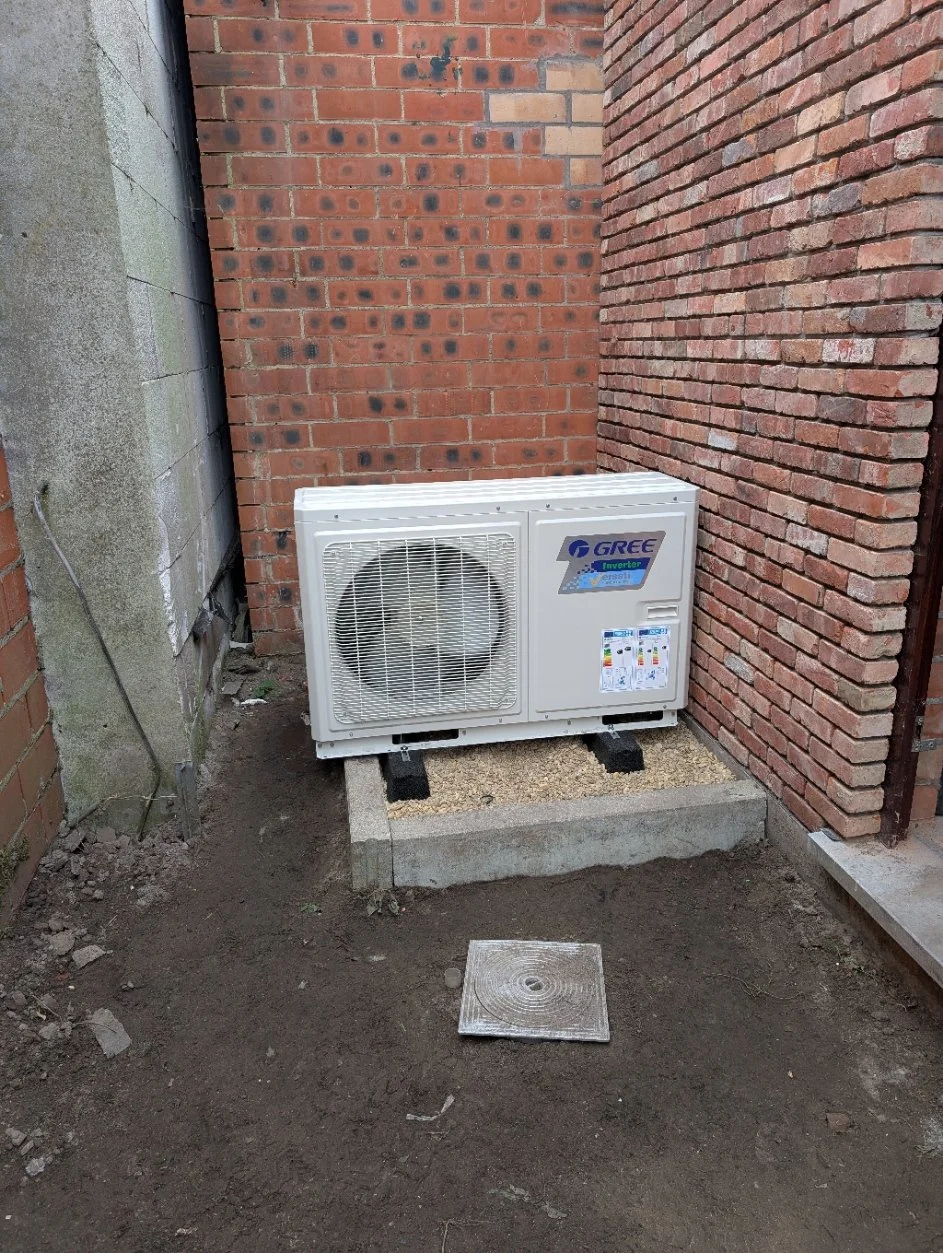 Een buitenunit van een airconditioningsysteem geplaatst op een betonnen plaat tussen bakstenen muren.
