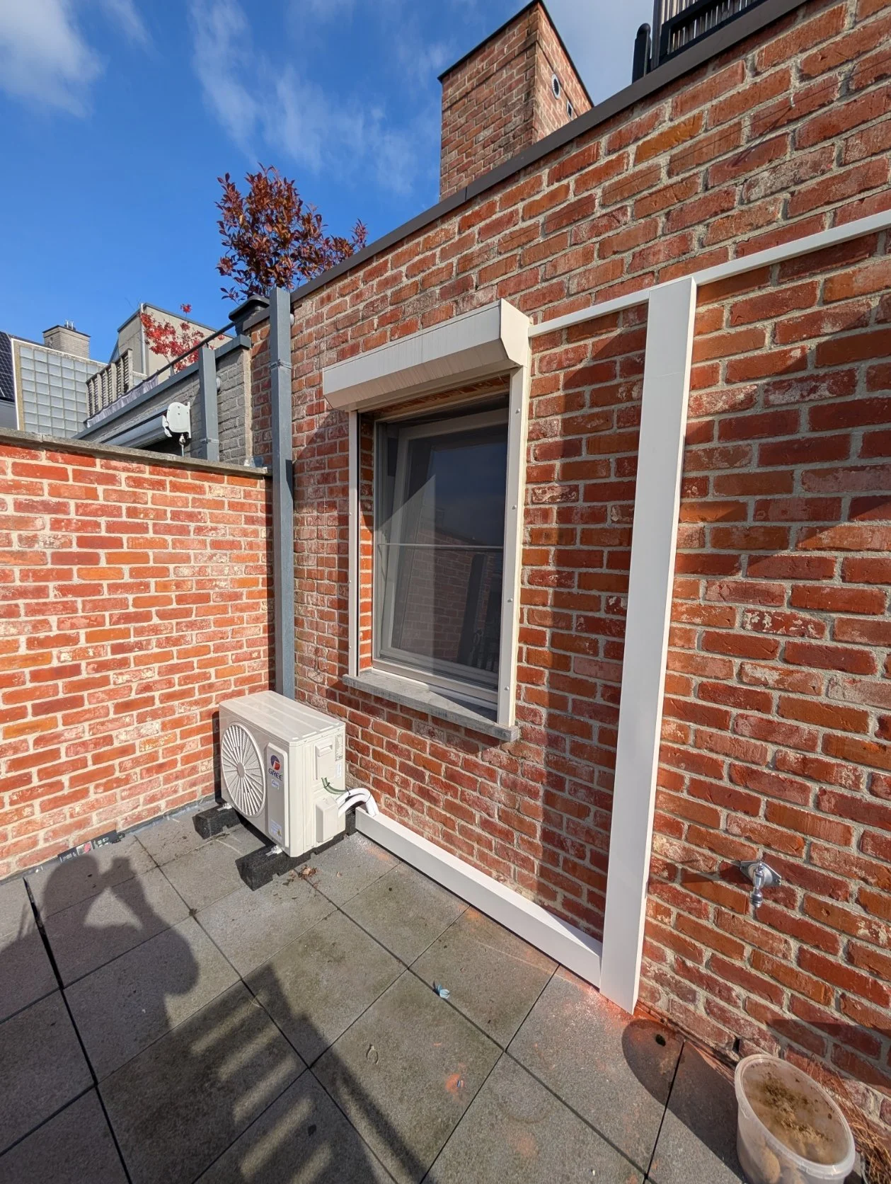 Buitenruimte van een appartement met een bakstenen muur, een raam met luifel, airconditioningunit, waterkraan en een afwasbaar tegelvloer.