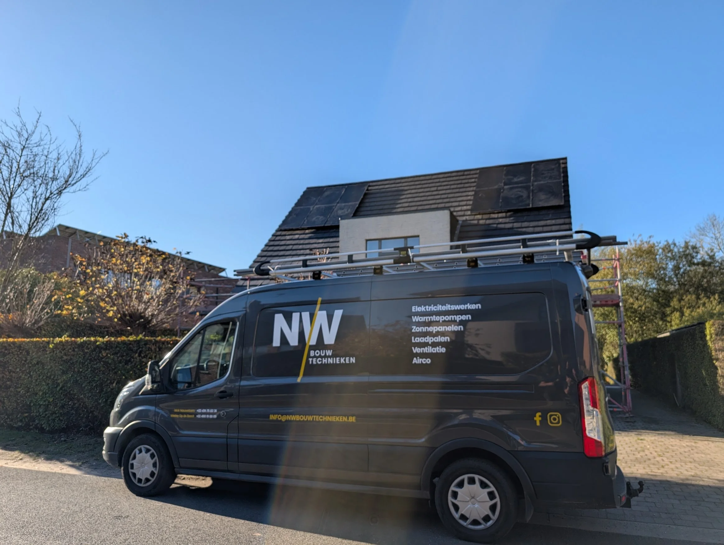 Een bedrijfswagen met de naam NW Bouw Technieken op een straat, met een ladder op het dak en een woning onder constructie of renovatie in de achtergrond.