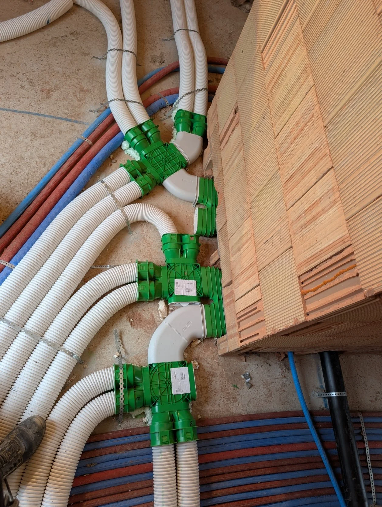 Installatie van witte en blauwe verwarmings- en waterleidingen met groene verbindingselementen op een bouwplaats, met bakstenen muur en vloer.