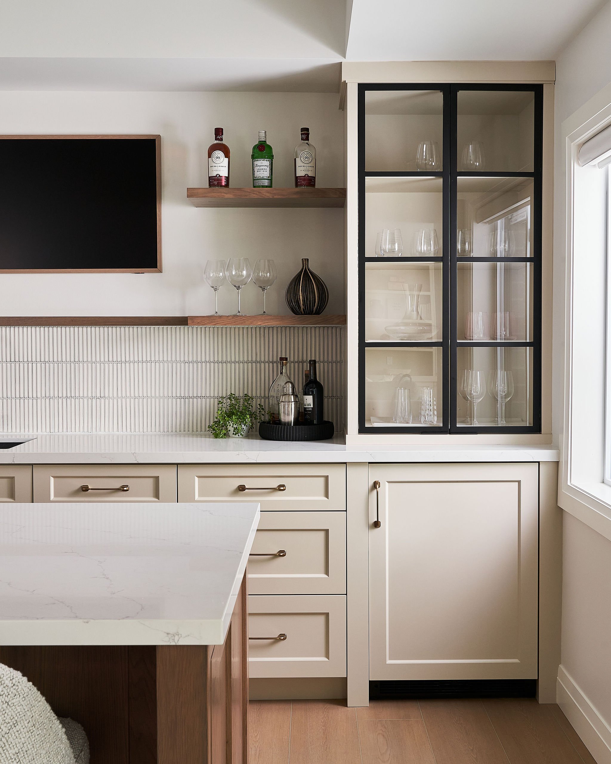 Basement bar featuring custom off-white cabinetry, metal and glass upper cabinets, warm wood open shelves and island with white quartz countertops by Studio Moffatt, London, Ontario
