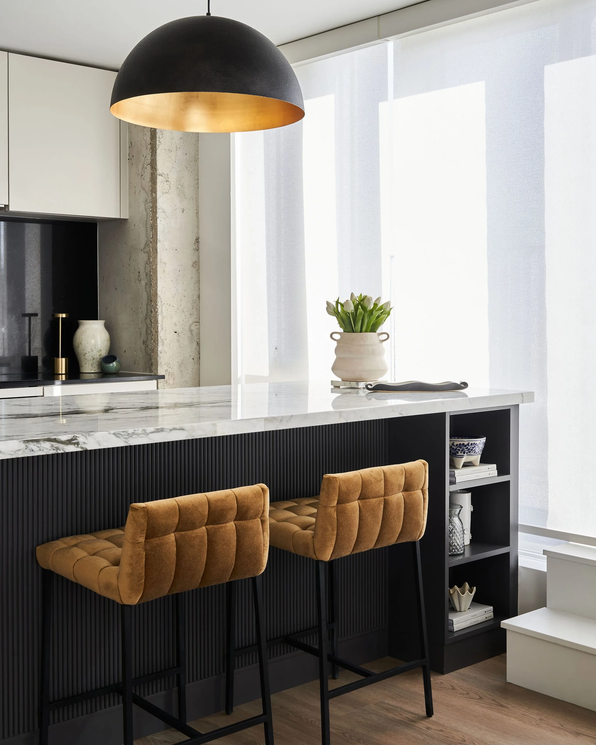 Toronto condo with upgraded custom charcoal kitchen island with reeded detailing, accompanied with velvet cognac bar stools and large black and brass pendant by Studio Moffatt