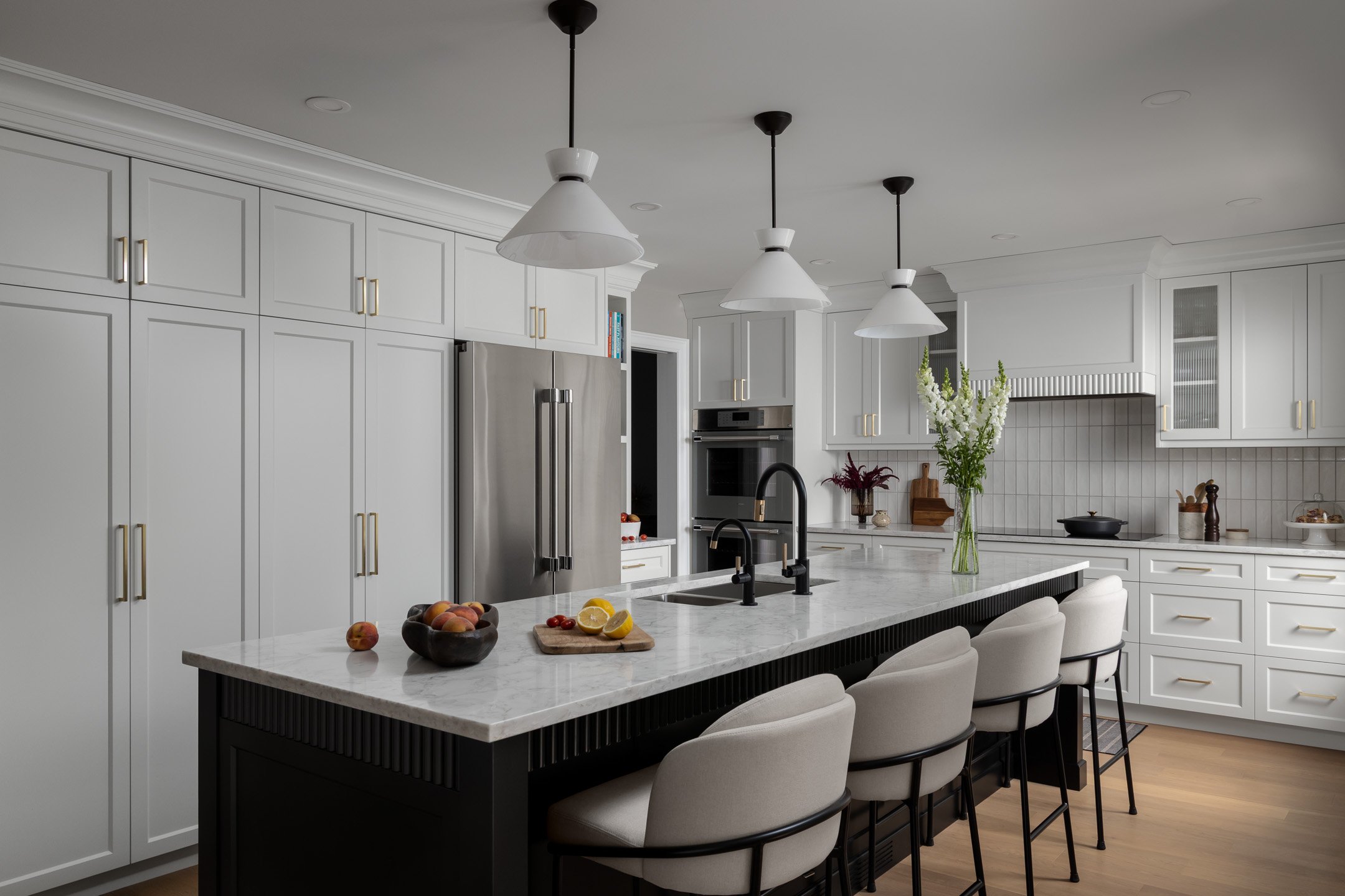 Residential renovation featuring a kitchen remodel with custom white cabinetry, a black kitchen island, custom range hood and quartz countertops.  Interior Design project by Studio Moffatt in London, Ontario