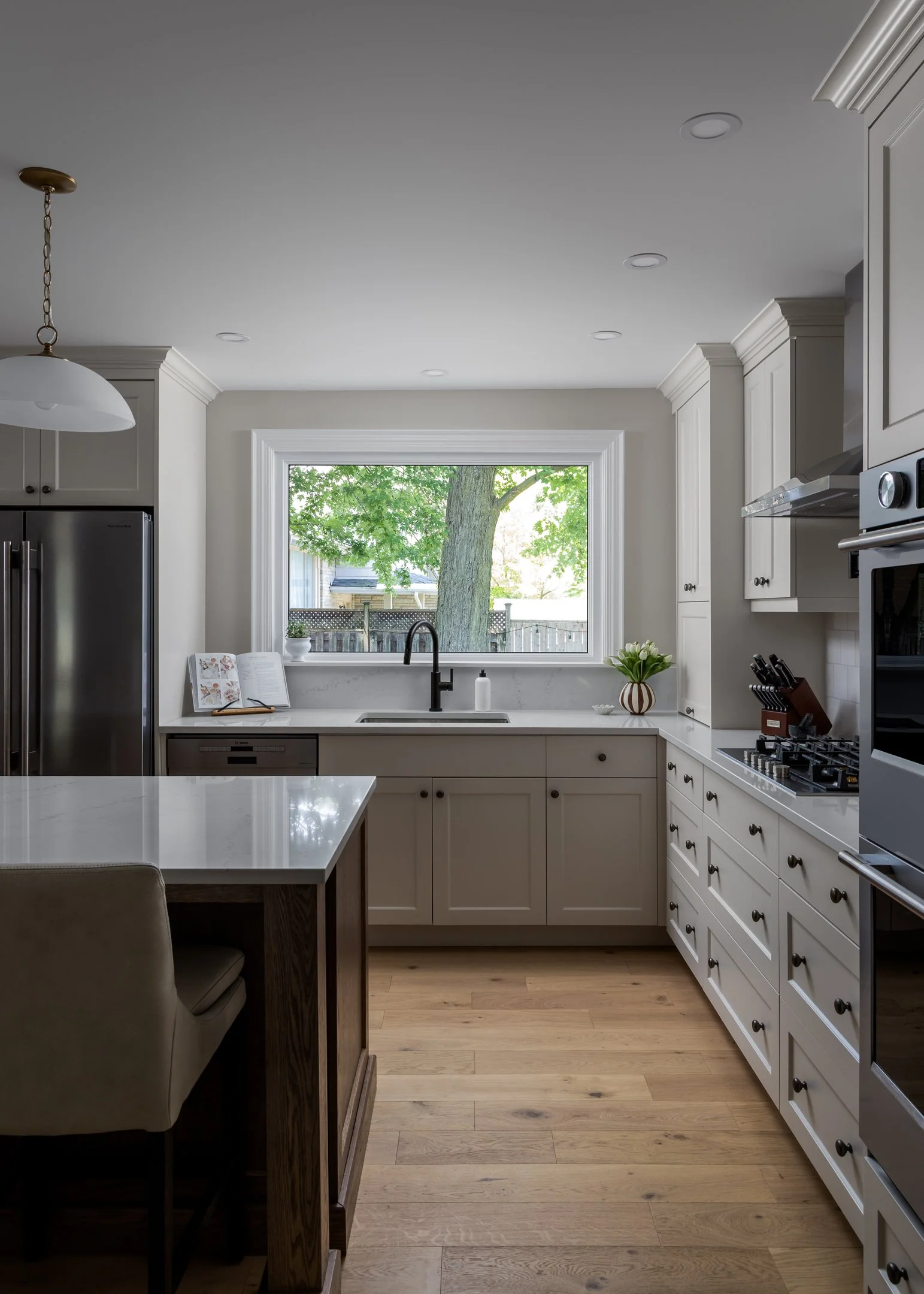 Custom transitional and timeless kitchen with off-white bespoke cabinetry, white quartz countertops, zelliege wall tile, white oak flooring and glass pendants by Studio Moffatt in London, Ontario