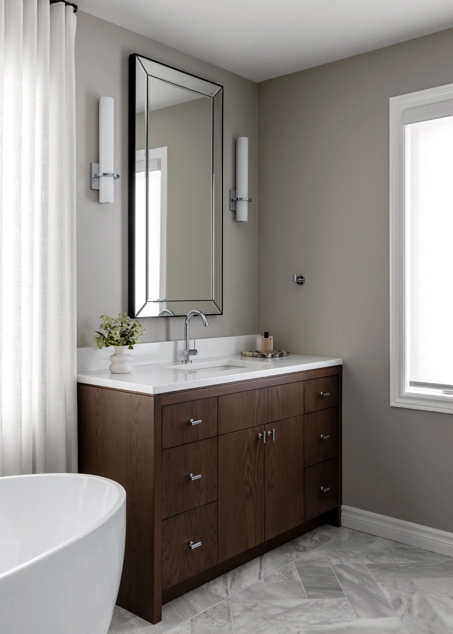 Timeless and elegant primary ensuite renovation featuring herringbone marble floors, a custom stained red oak vanity with a white quartz countertop, custom full length drapery by Studio Moffatt