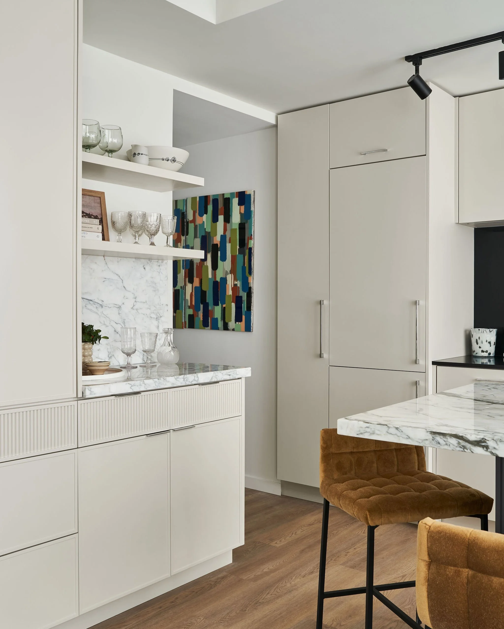 Arabescato Vagli marble countertops and backsplash sit on custom cabinetry.  Colourful abstract artwork brings in a pop of colour against a neutral palette