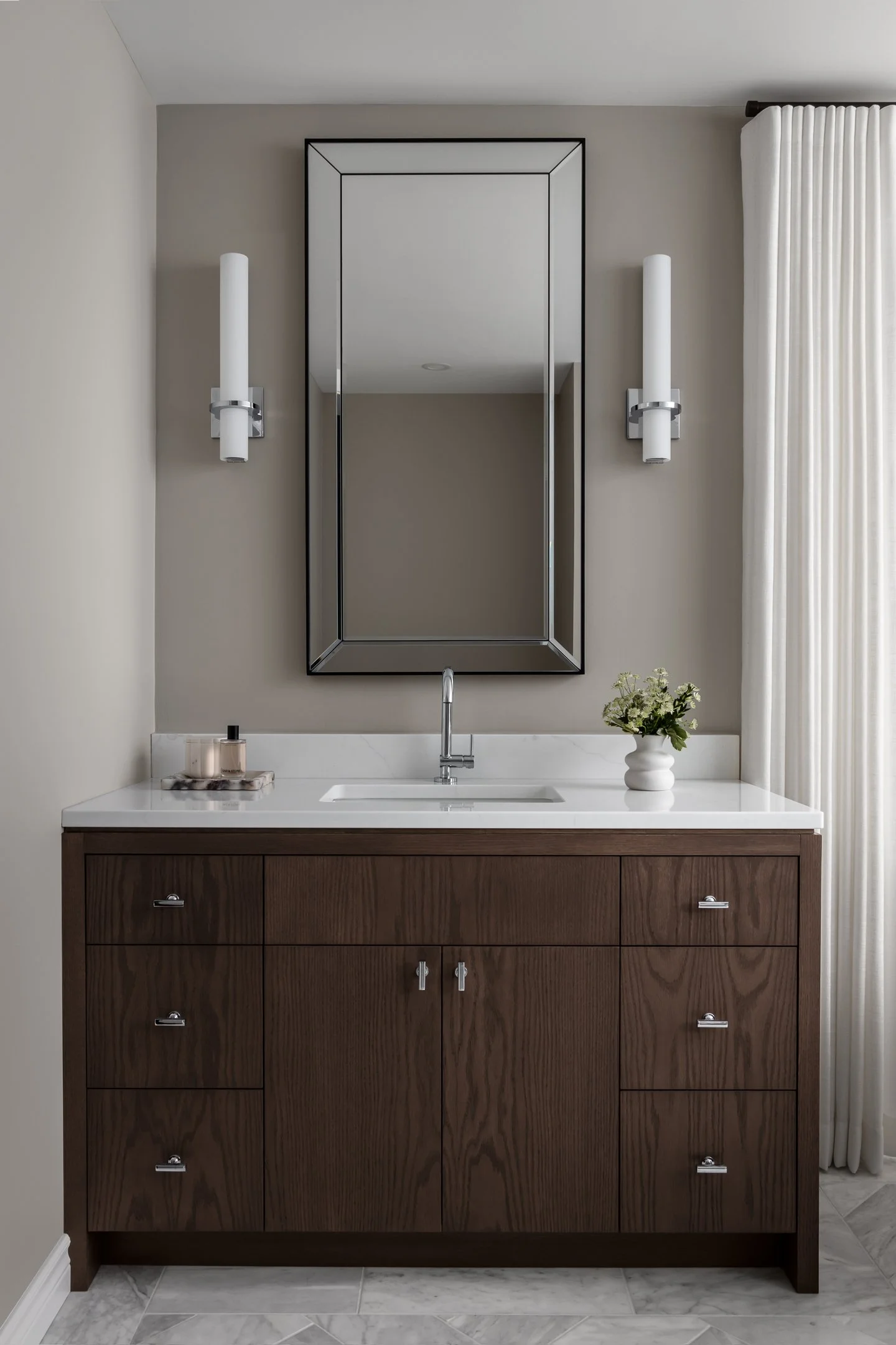 Timeless and elegant primary ensuite renovation featuring a custom stained red oak vanity with a white quartz countertop, sconces and oversized mirror y by Studio Moffatt