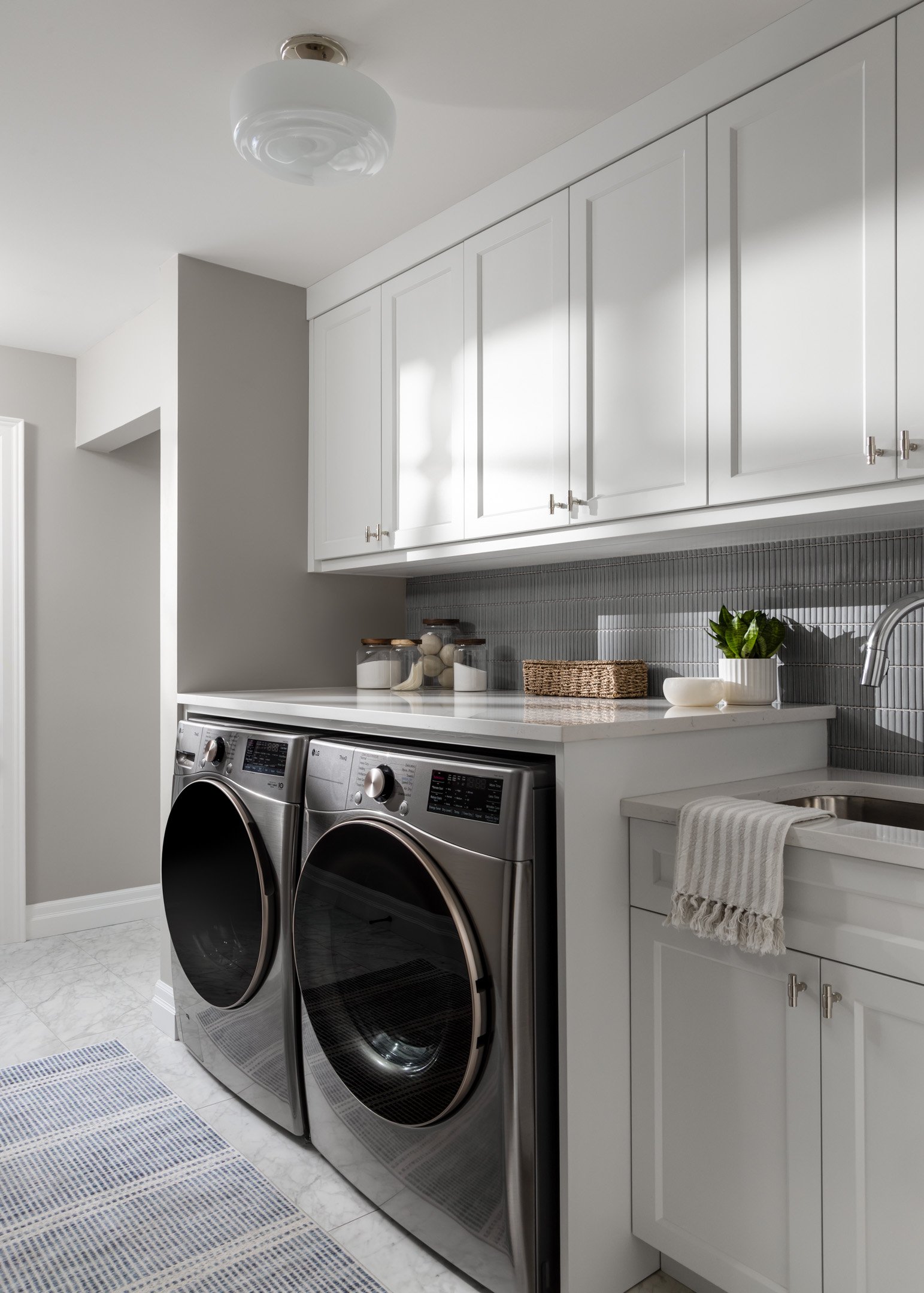 Remodeled laundry room with custom white cabinetry, white quartz countertops, blue kit-kat backsplash and porcelain tile flooring by Studio Moffatt in London, Ontario