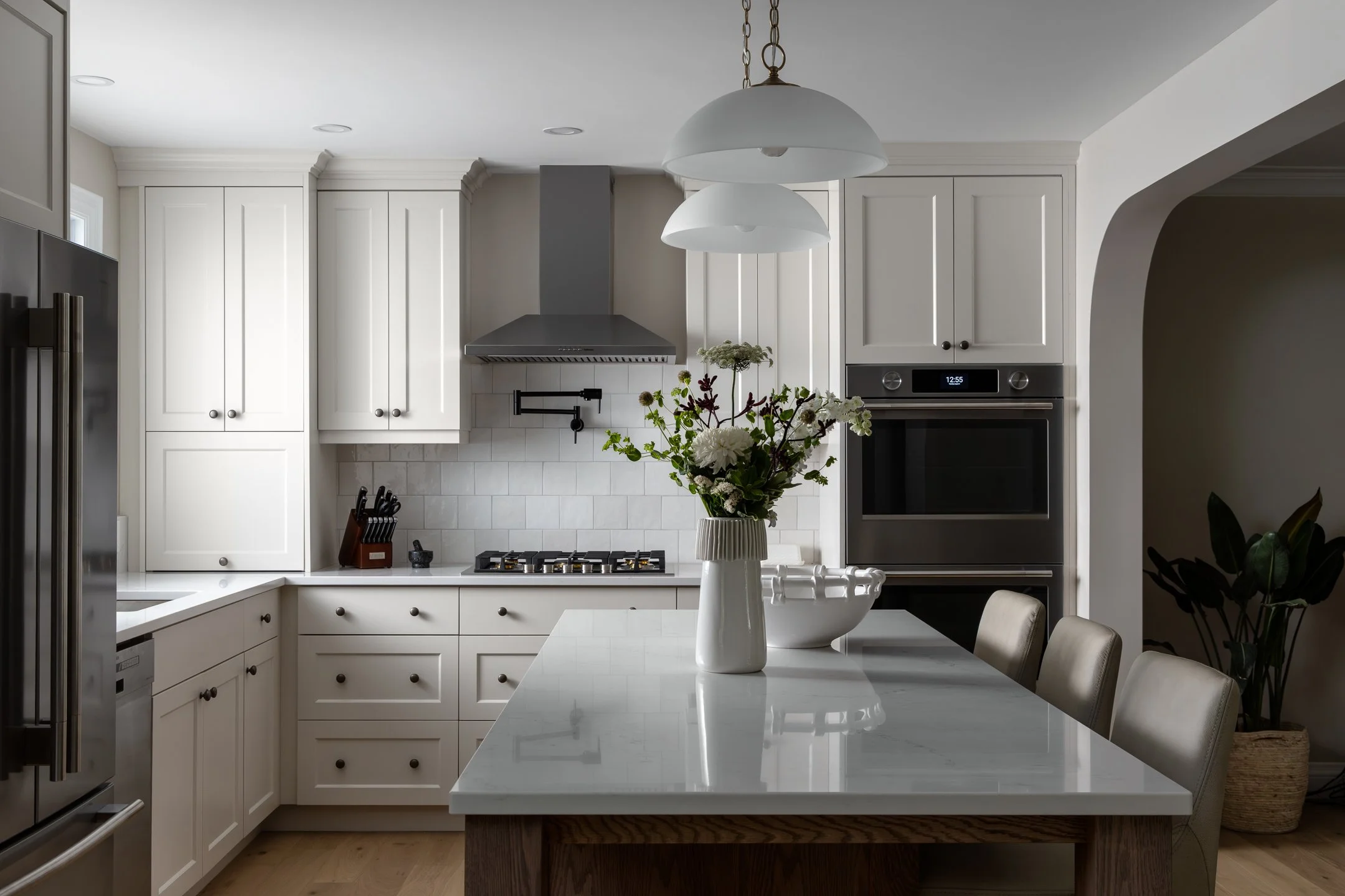 Custom transitional and timeless kitchen with off-white bespoke cabinetry, white quartz countertops, zelliege wall tile and glass pendants by Studio Moffatt in London, Ontario