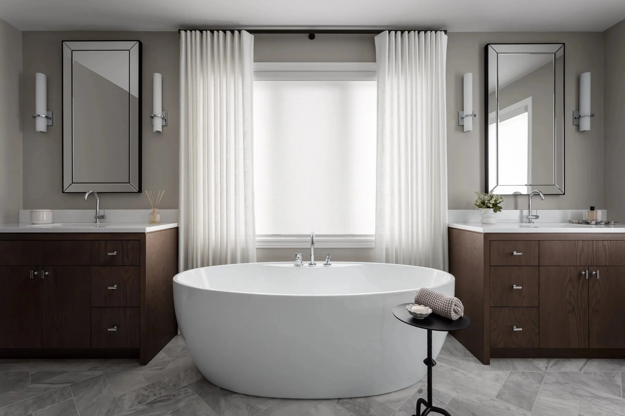 Classic ensuite design featuring a freestanding bath tub framed by two stained red oak vanities, white quartz countertops and chrome fixtures. 