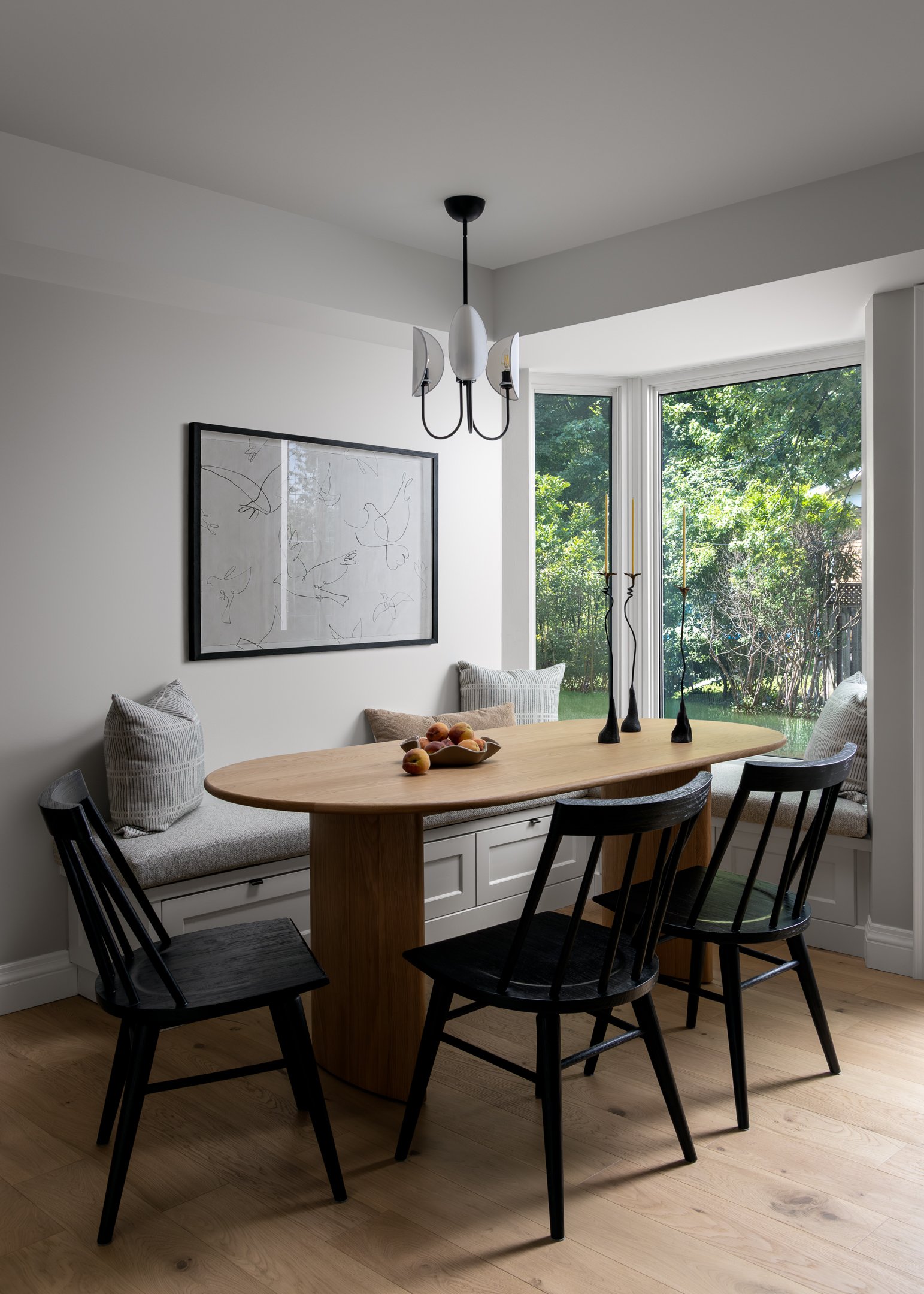 Dining area breakfast nook for a busy family! The space features bespoke banquette seating below a bay window, accompanied with textured cushion, white oak table and black transitional chairs, by Studio Moffatt in London, Ontario