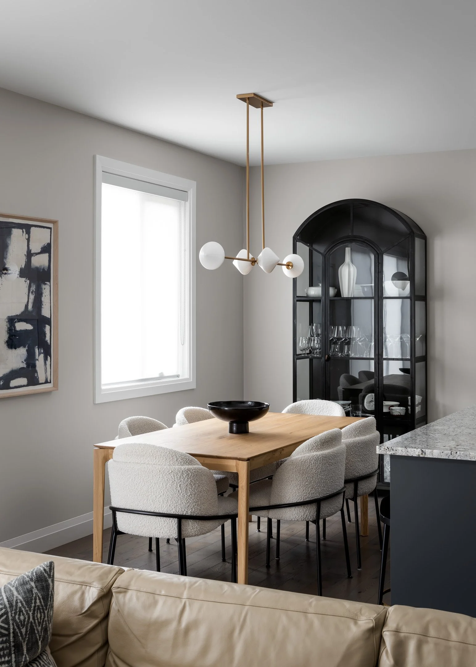 Modern dining room with white oak table, textured ivory upholstered dining chairs, glass and metal display cabinet and sculptural linear pendant by Studio Moffatt, London, Ontario