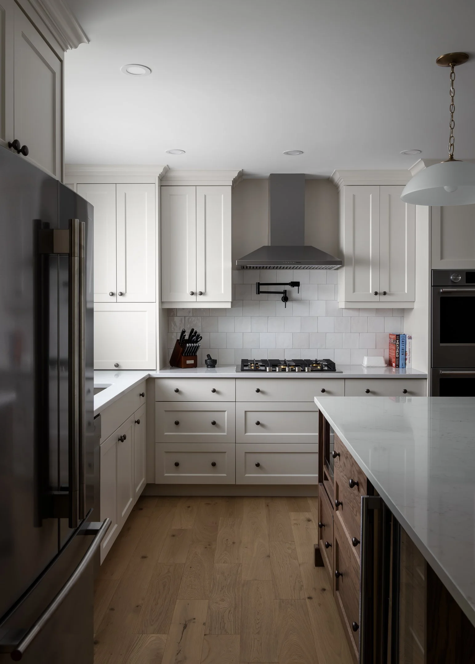 Custom transitional and timeless kitchen with off-white bespoke cabinetry, white quartz countertops, zelliege wall tile and glass pendants by Studio Moffatt in London, Ontario