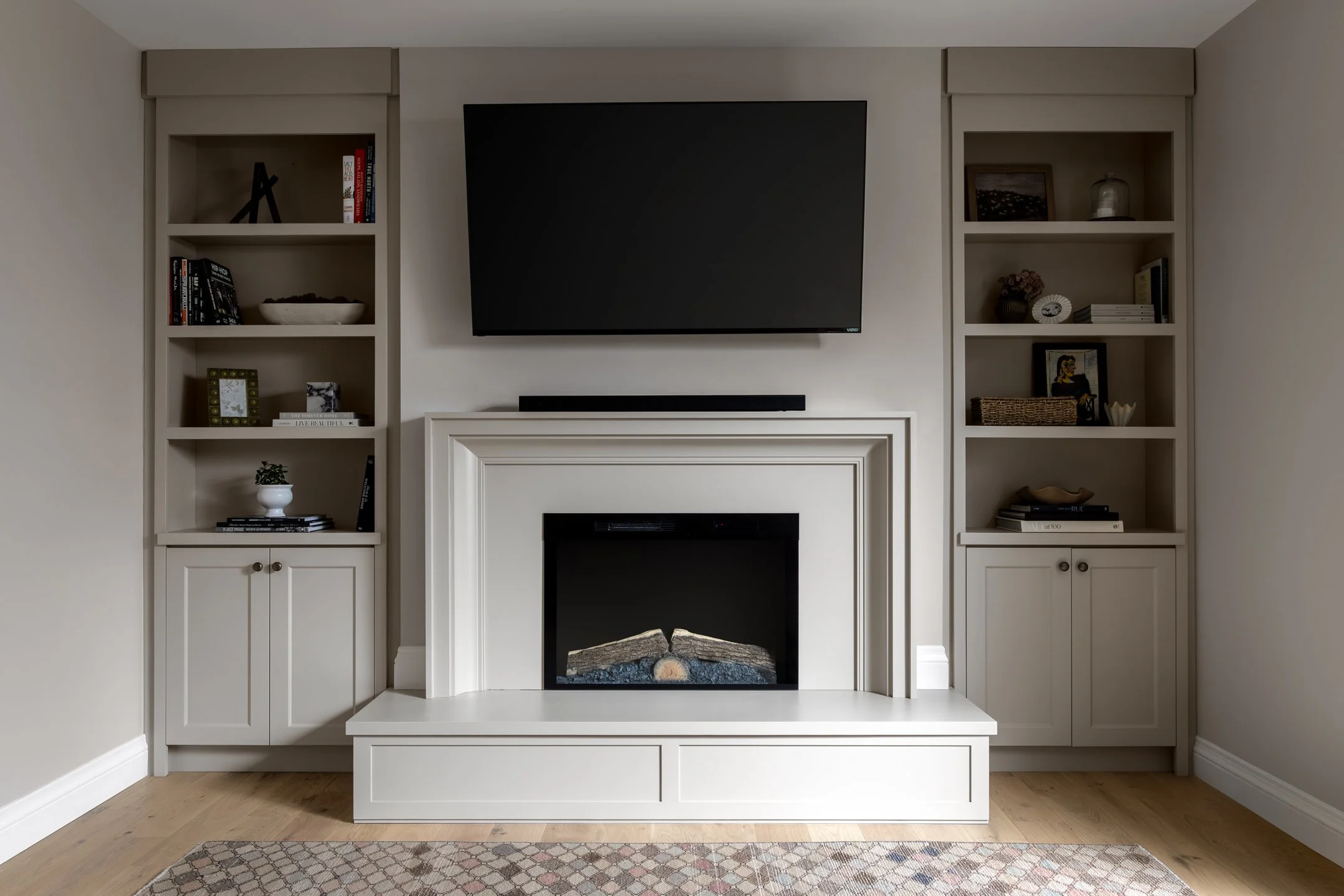 Fireplace design with off-white built-ins framing an elegant and modern fireplace on raised hearth by Studio Moffatt in London, Ontario