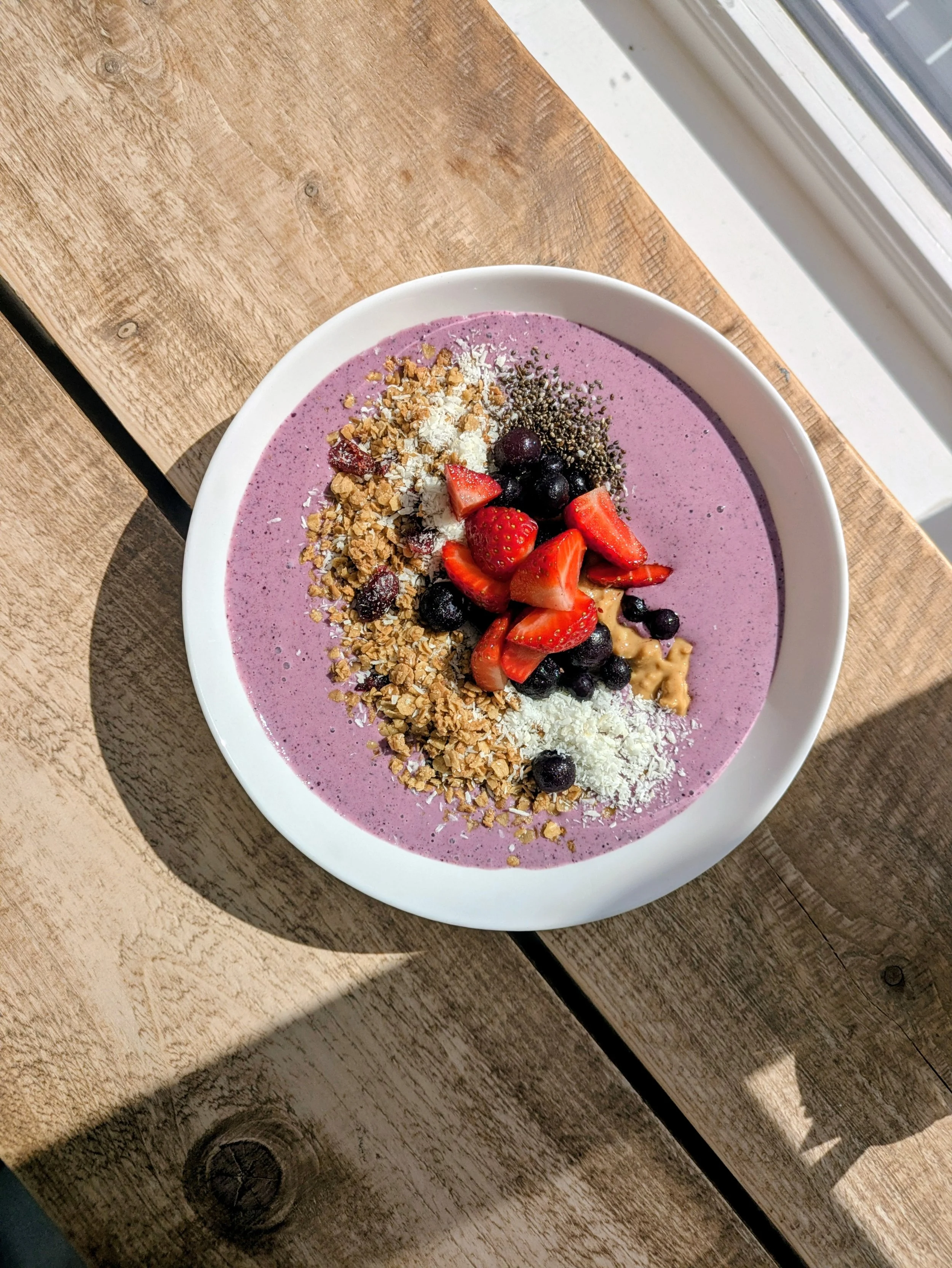 Bowl of pink smoothie topped with granola, strawberries, blueberries, shredded coconut, and chia seeds.  Smokthie bowl. Healthy breakfast options available on the brunch menu.