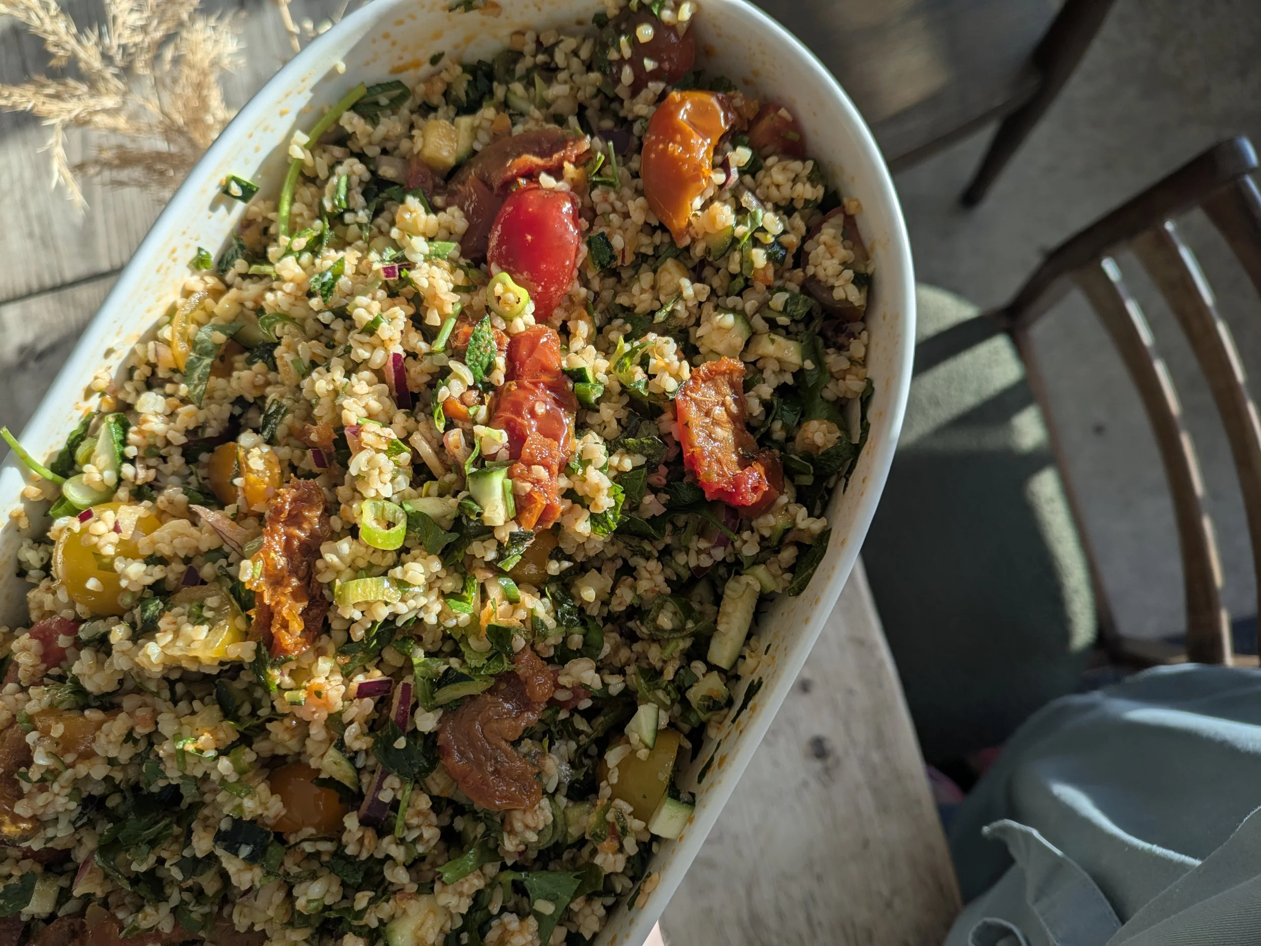 A dish of grain salad with tomatoes, chopped green onions, herbs, and possibly sun-dried tomatoes, served in a white oval bowl.