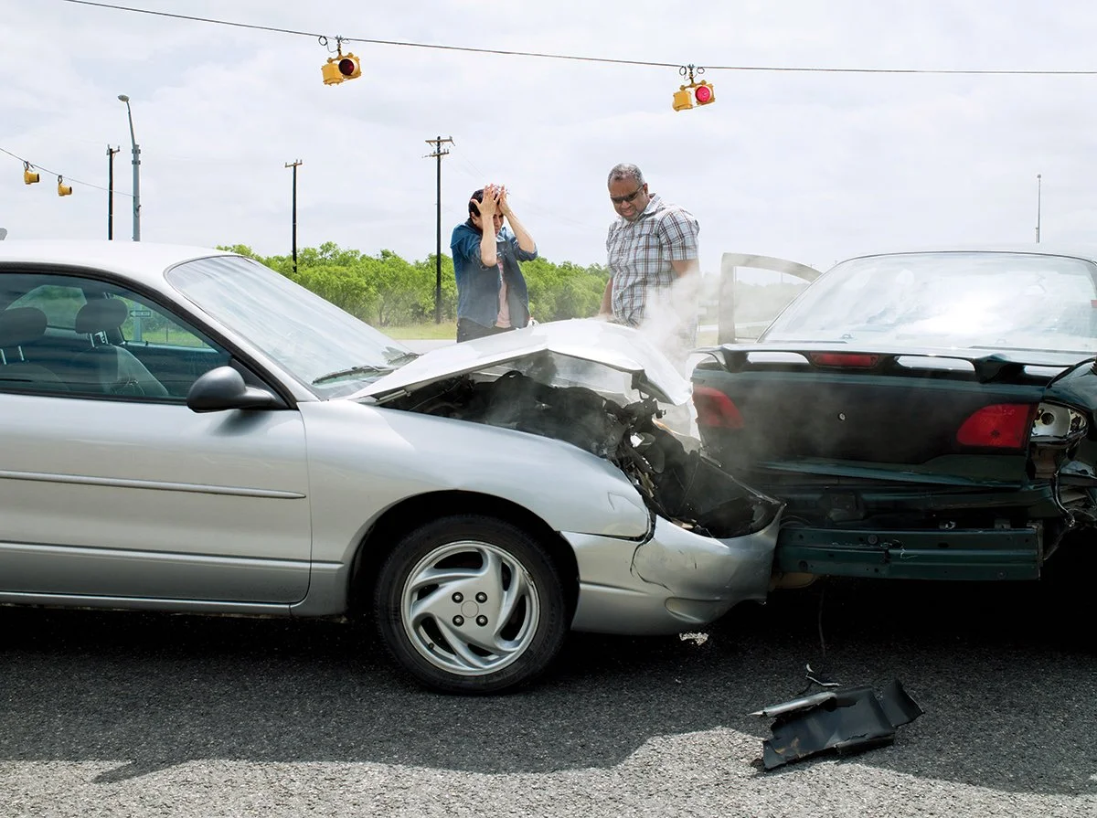 A car crash with two frustrated drivers standing roadside.