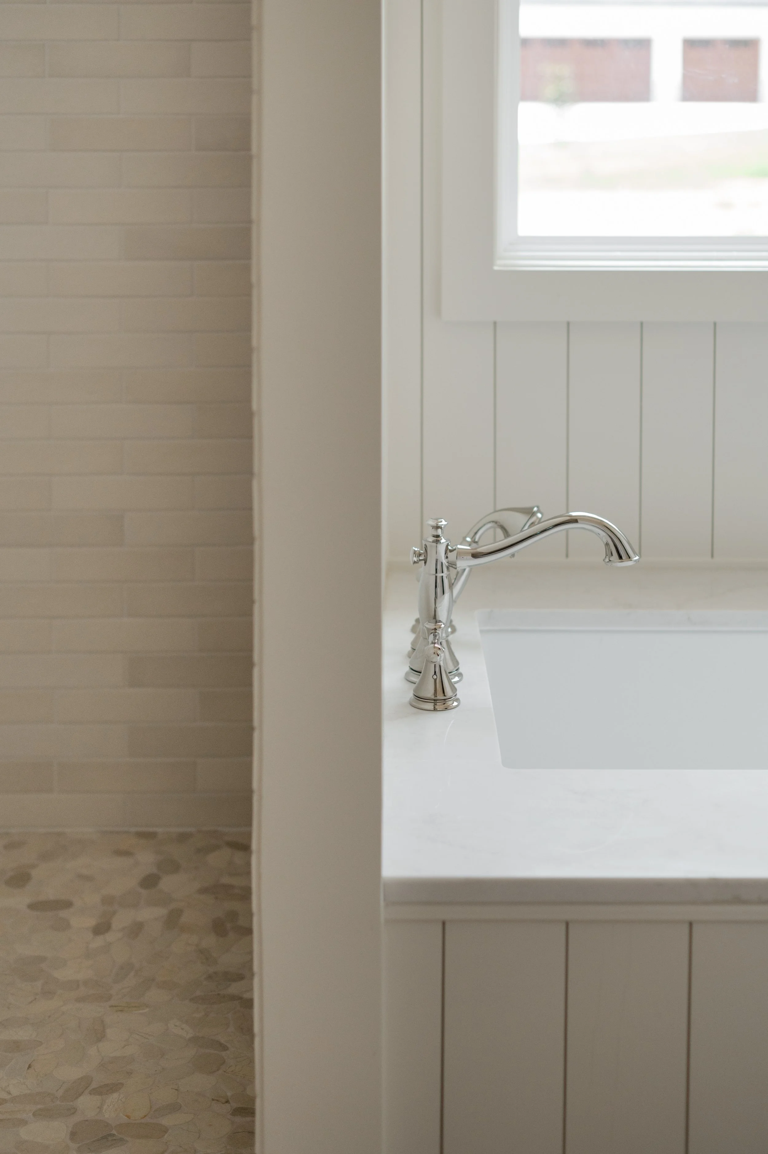 Bathroom with a white marble countertop, silver faucet, and a white bathtub, with a window above.