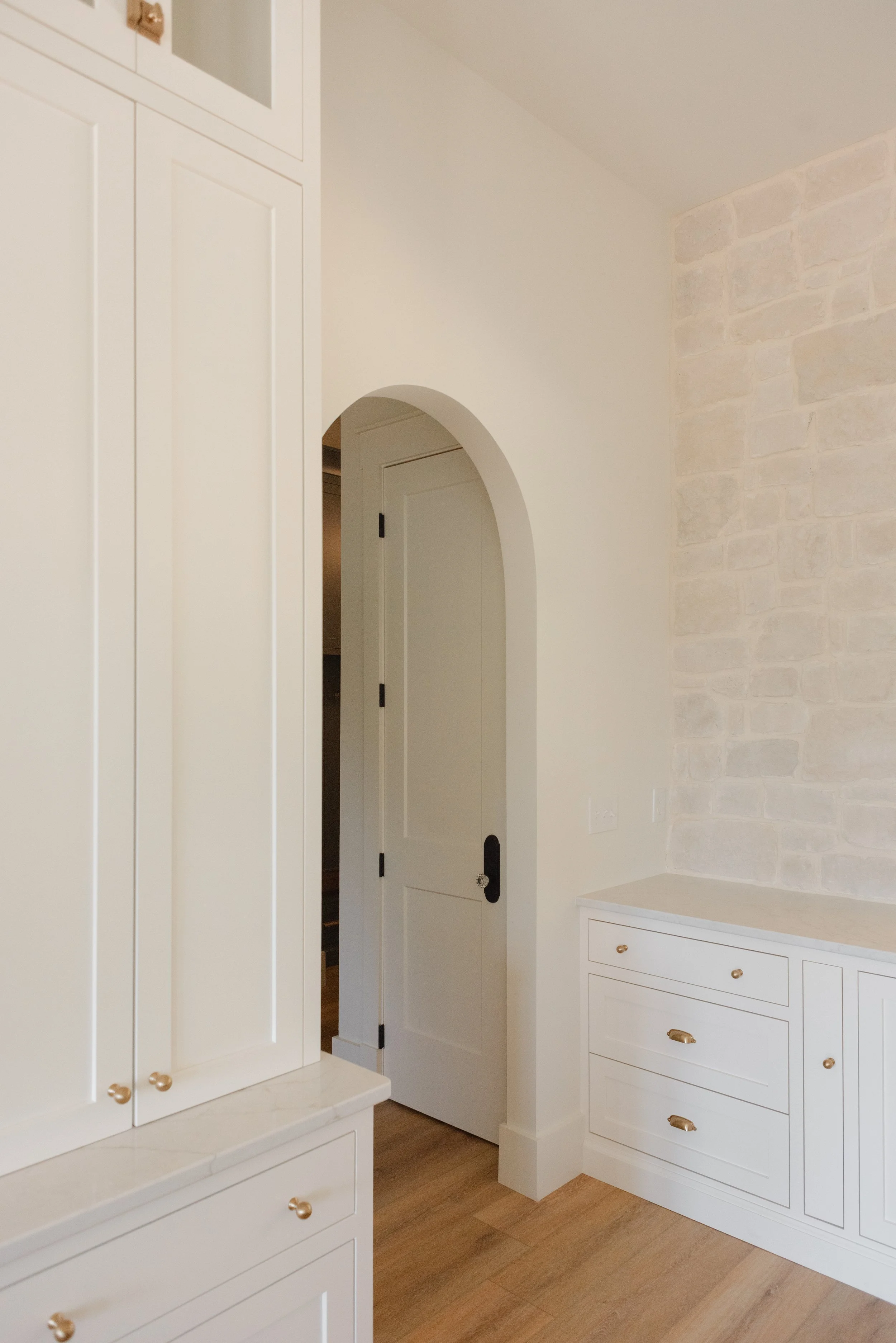 Custom interior space designed by Knoxville custom home builder Wiersma Homes, showcasing white cabinetry, a stone accent wall, black door handle, and arched doorway for an elevated, timeless feel.