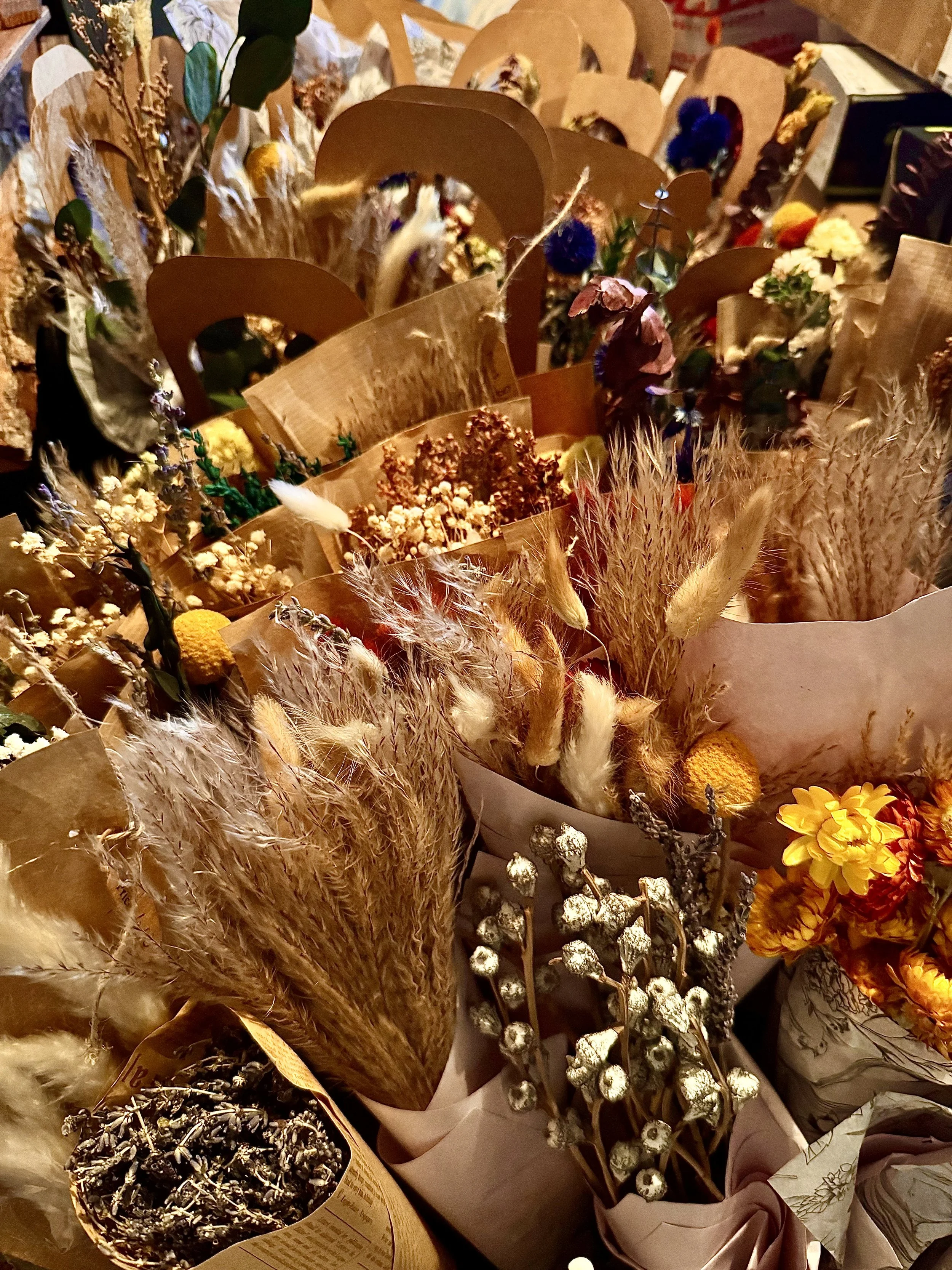 A display of various dried flowers and plants arranged in bouquets and containers, including pampas grass and other dried florals.