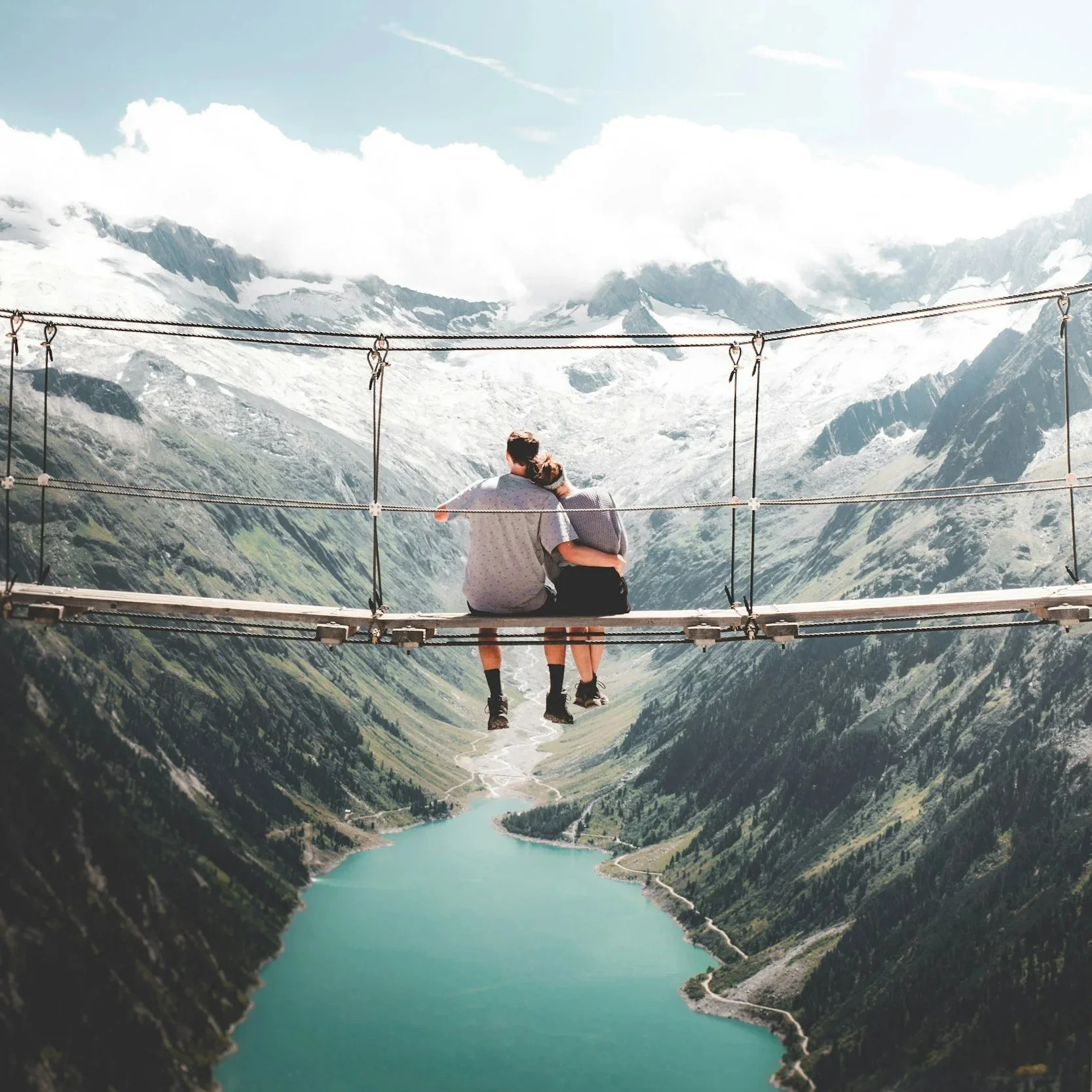 couple hugging each other as they sit on a bridge and look out at moutains and river