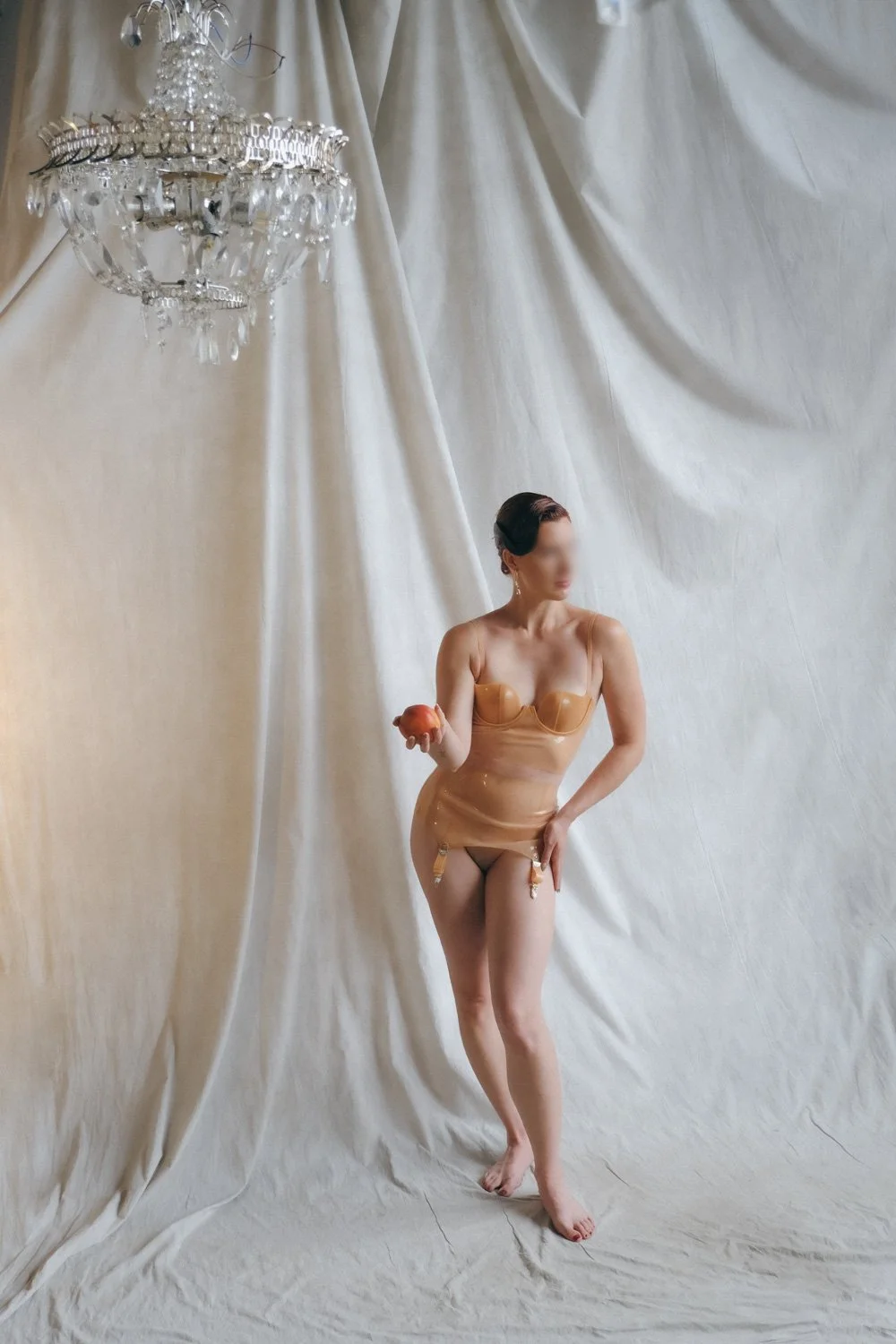 NYC Kinky Redhead Escort Julia Flowerbomb posing in transparent latex and holding a peach.