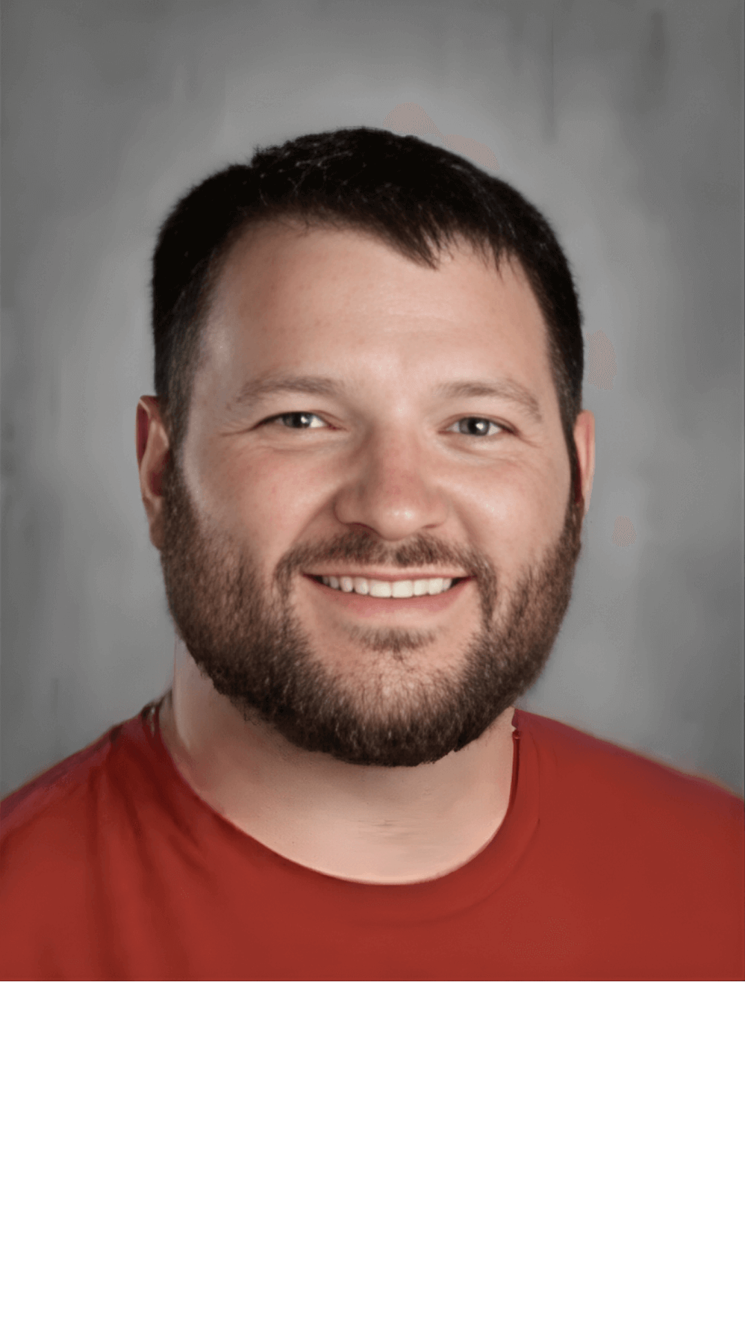 A portrait photograph of a smiling man with short dark hair, a beard, and a mustache, wearing a red shirt.