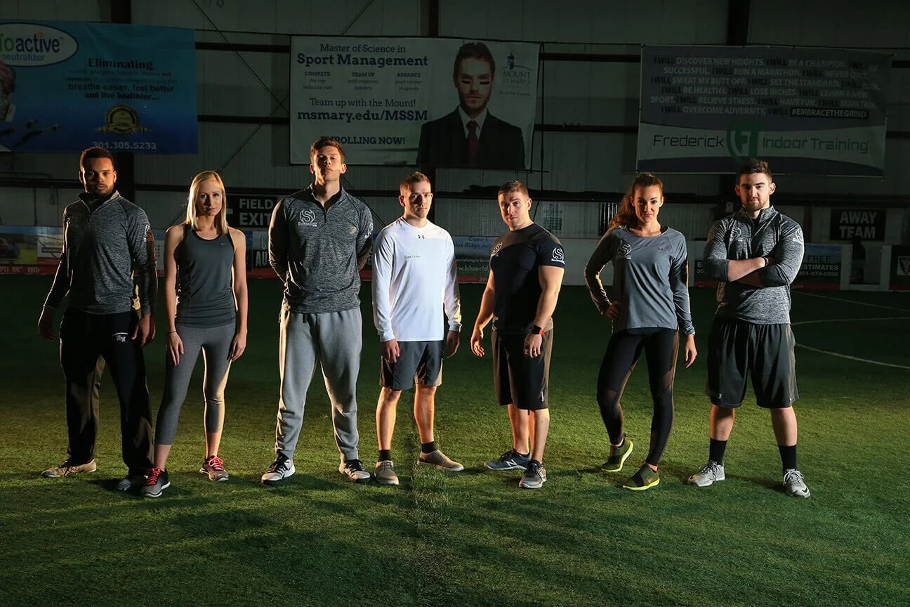 Fitness photography photoshoot in Maryland gym. Group of seven athletes standing on an indoor field.