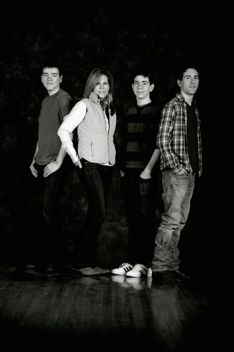 Black and white photo of four teenagers standing in a line with a dark background.
