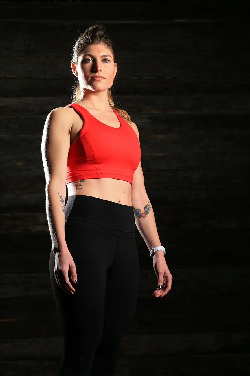 Woman in red sports bra and black leggings standing against dark background.