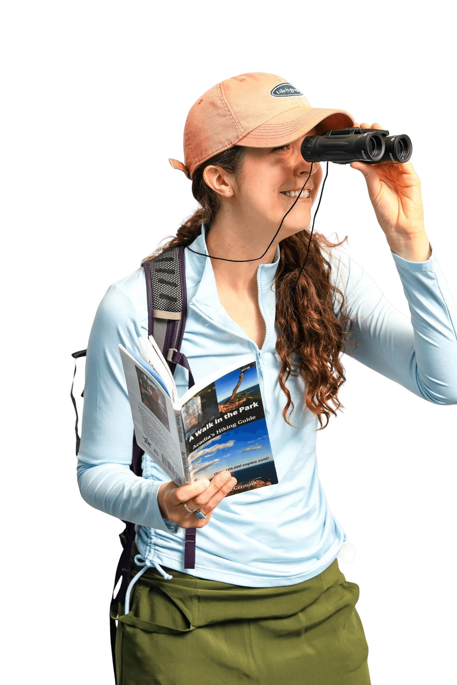 A woman in hiking gear looks through binoculars while holding a park guidebook, standing against a black background.
