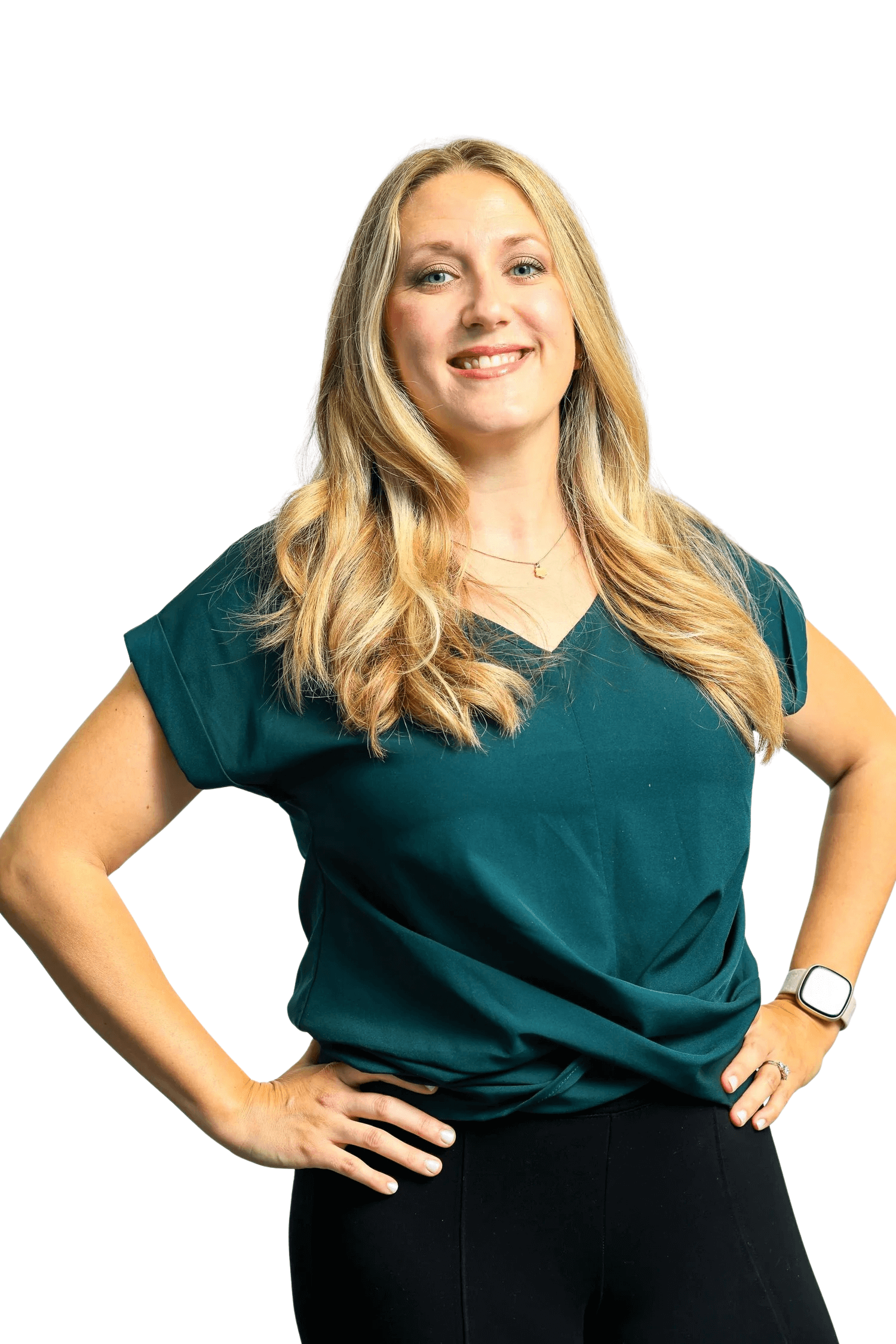 A smiling woman with long blonde hair, wearing a teal scrub top, black pants, a smartwatch, a ring, and a necklace, standing with her hands on her hips against a white background.