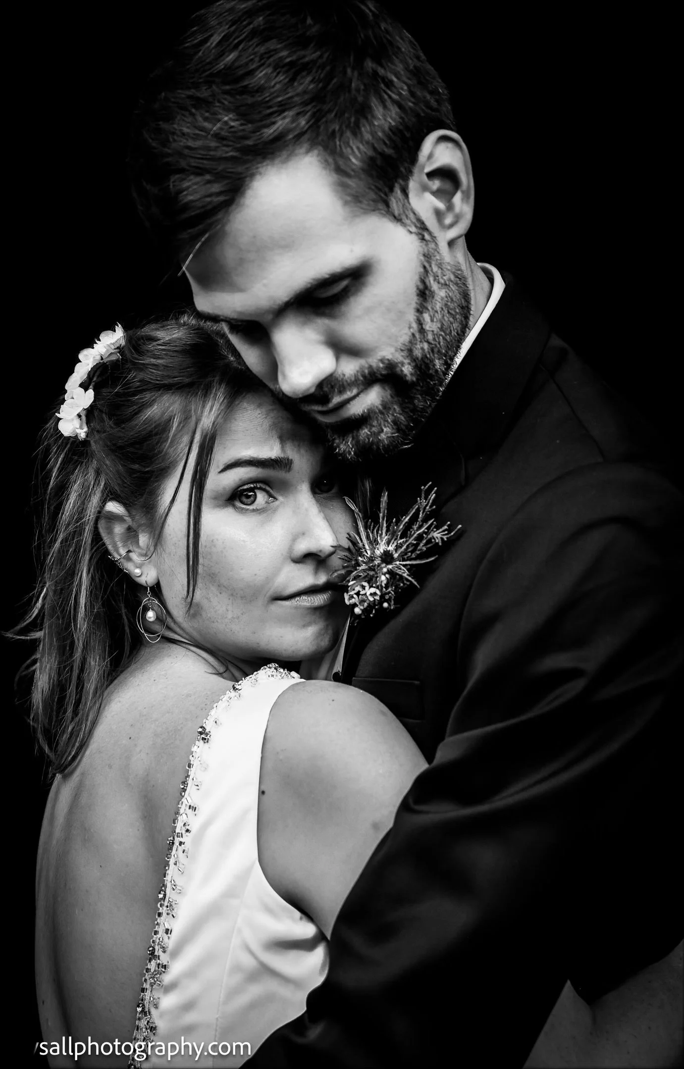 Black and white photo of a couple embracing closely, with the woman looking directly at the camera and the man looking downward, both with intense expressions.
