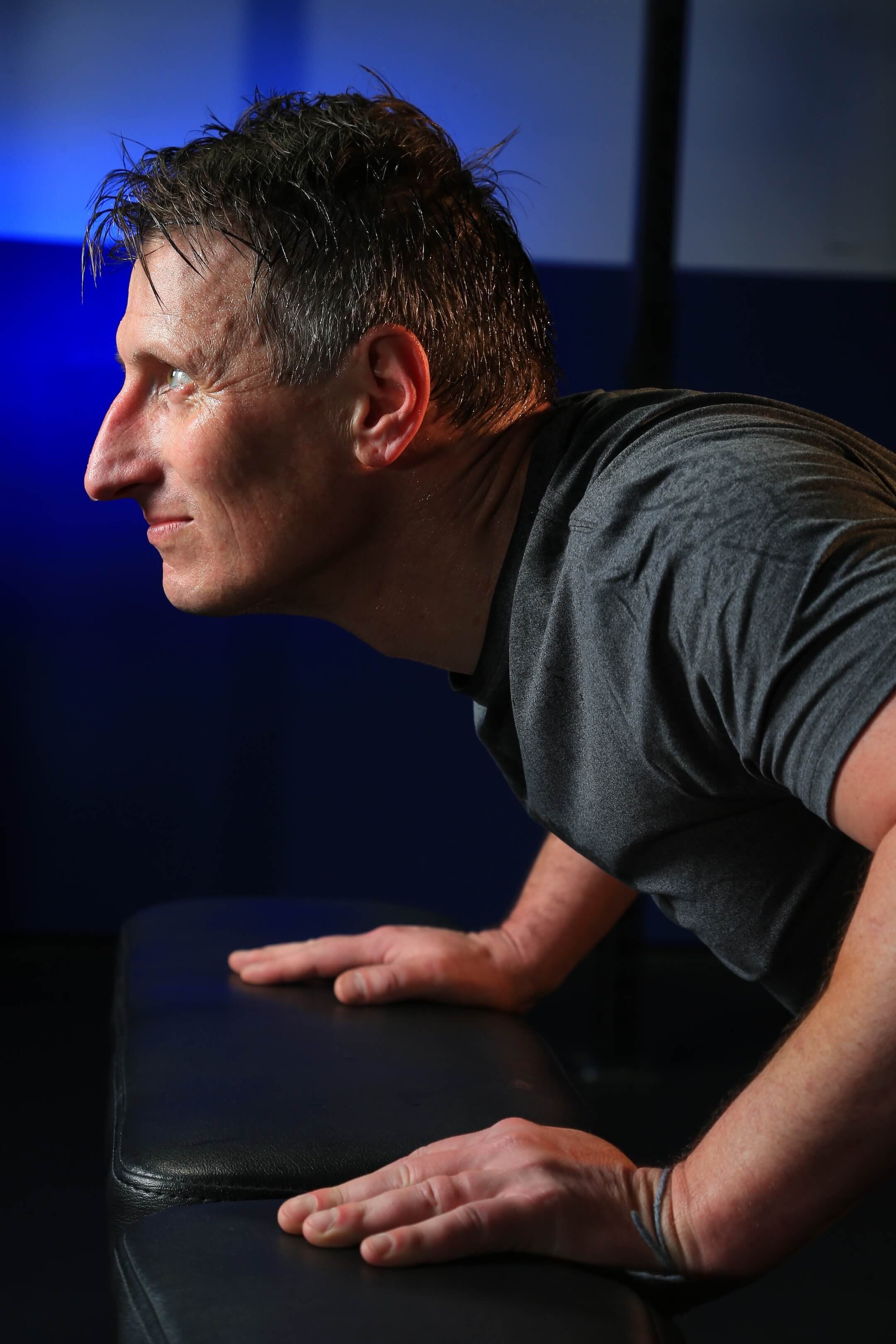 A man doing a push-up in a dark gym with blue lighting.