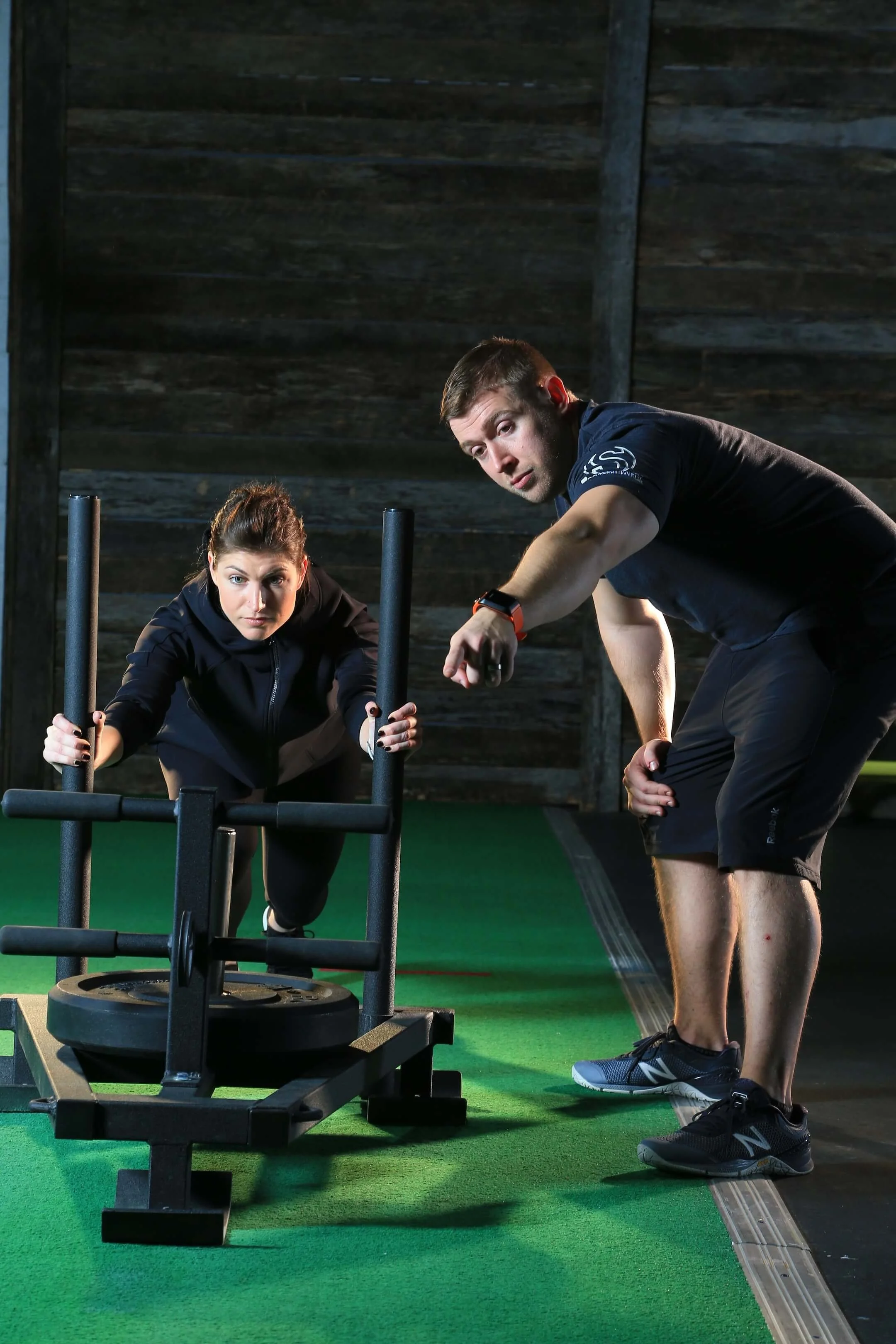 A man and woman working out with a sled push machine in a gym.