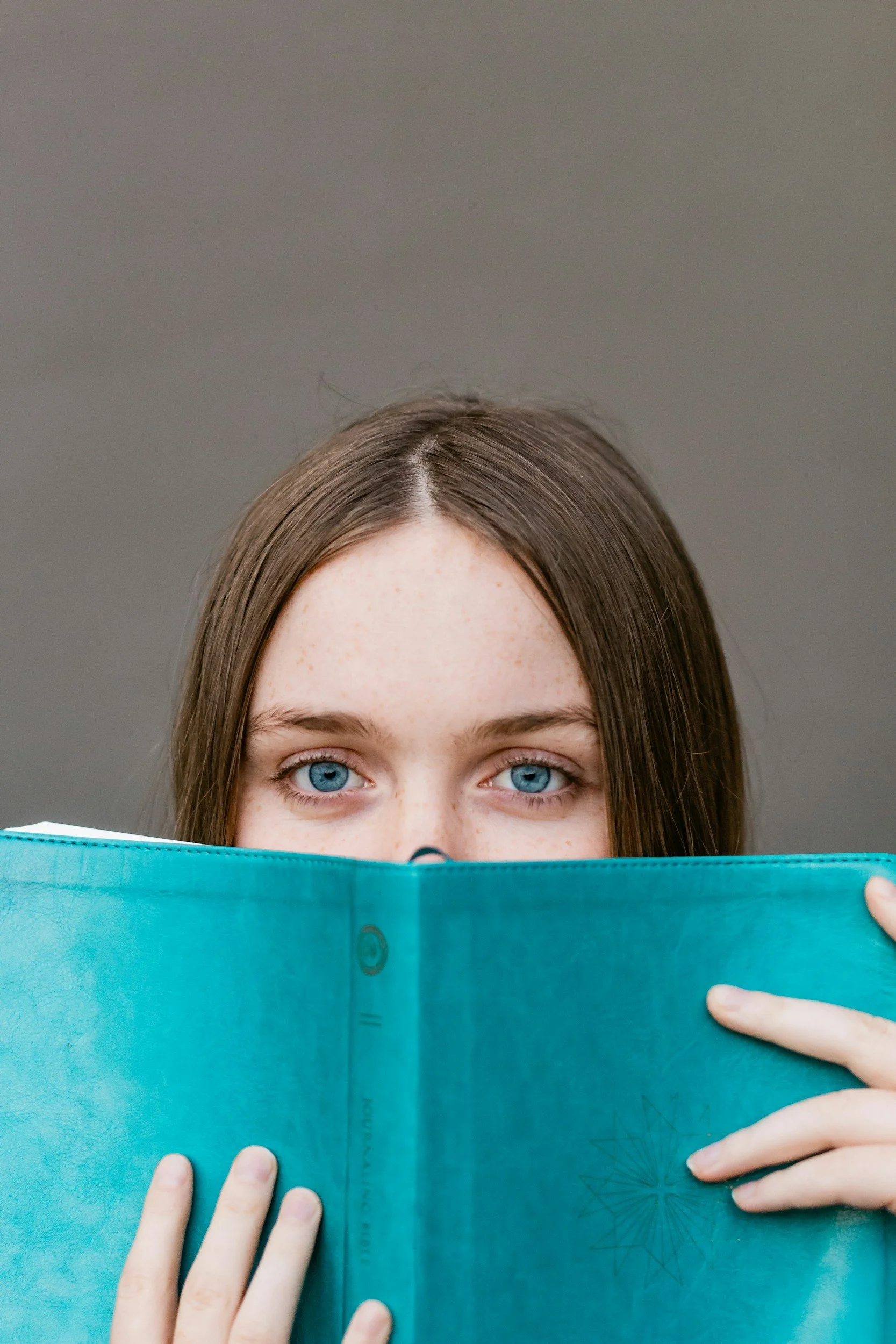 a girl peering over the top of a book