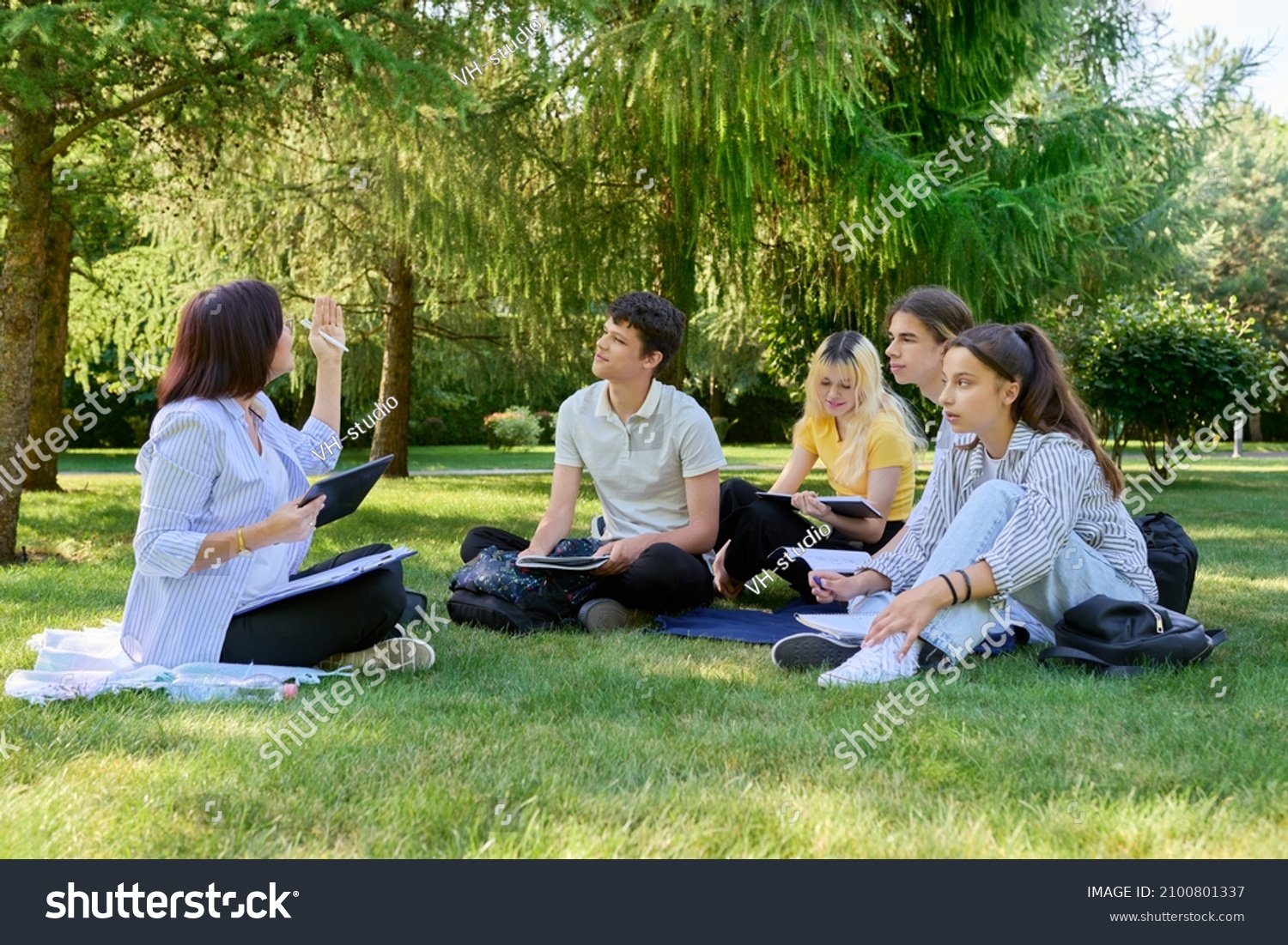 stock-photo-outdoor-group-of-students-with-female-teacher-sitting-on-grass-2100801337.jpg
