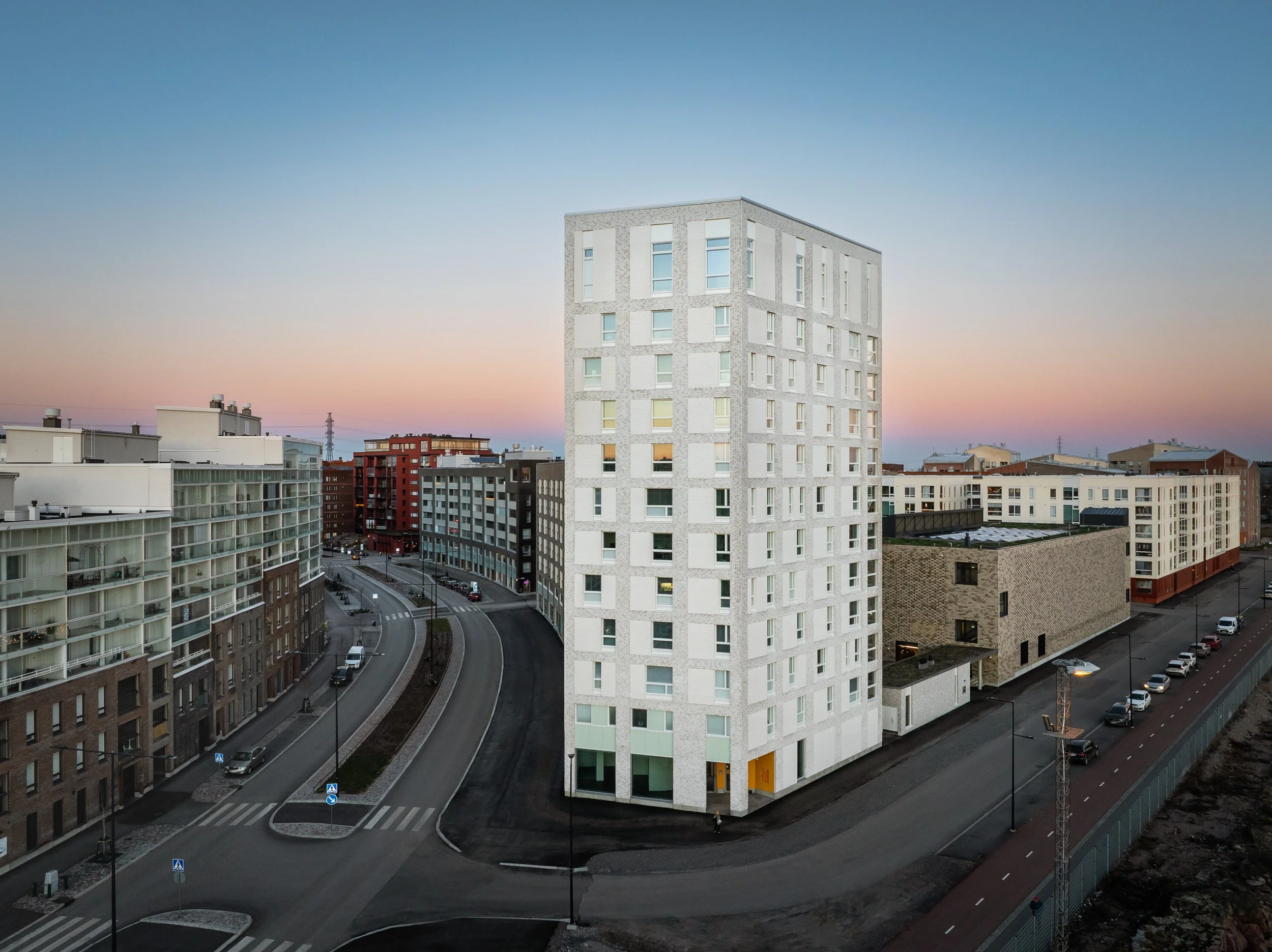 Vaalea tiilinen kerrostalo Helsingin Pasilan Postipuiston alueella auringonlaskuun kuvattuna.