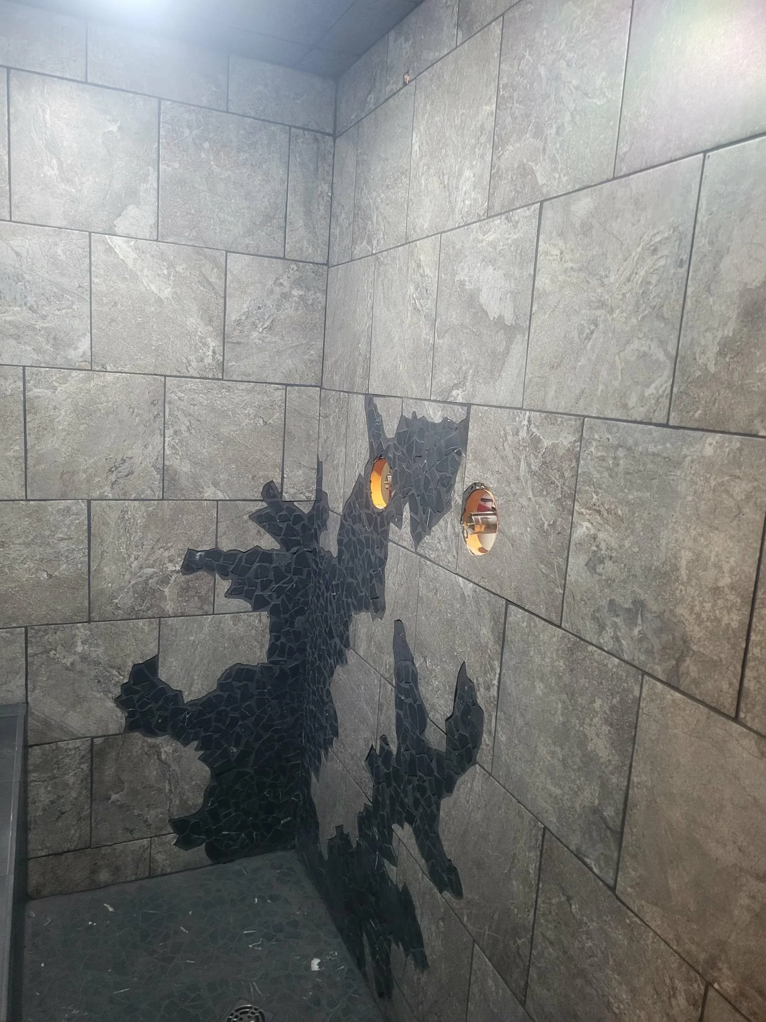 A black tile fractal mosaic on a tiled bathroom wall, ready for shower handles.